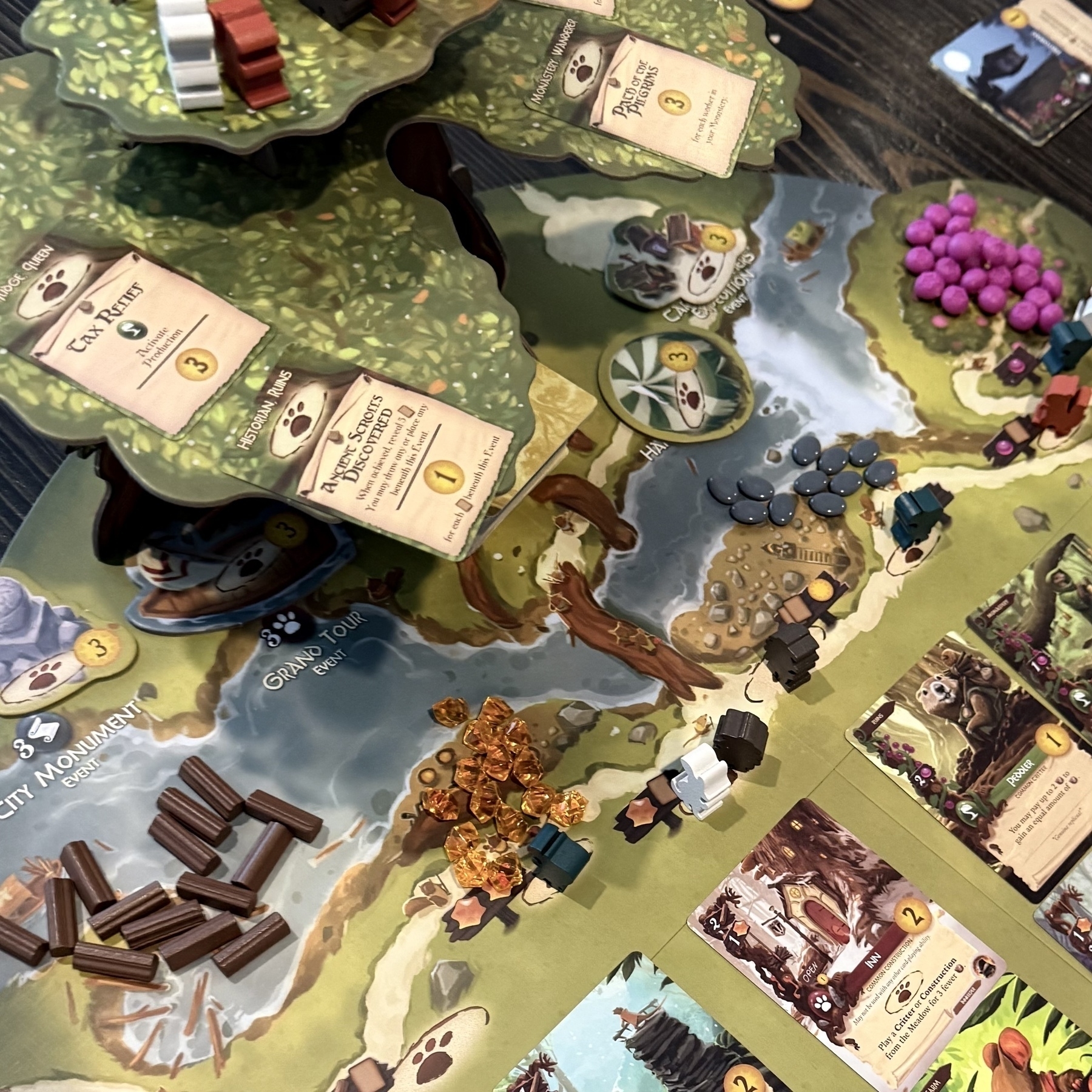 A tabletop game setup featuring a forest-themed board with cards, tokens, and game pieces arranged neatly.