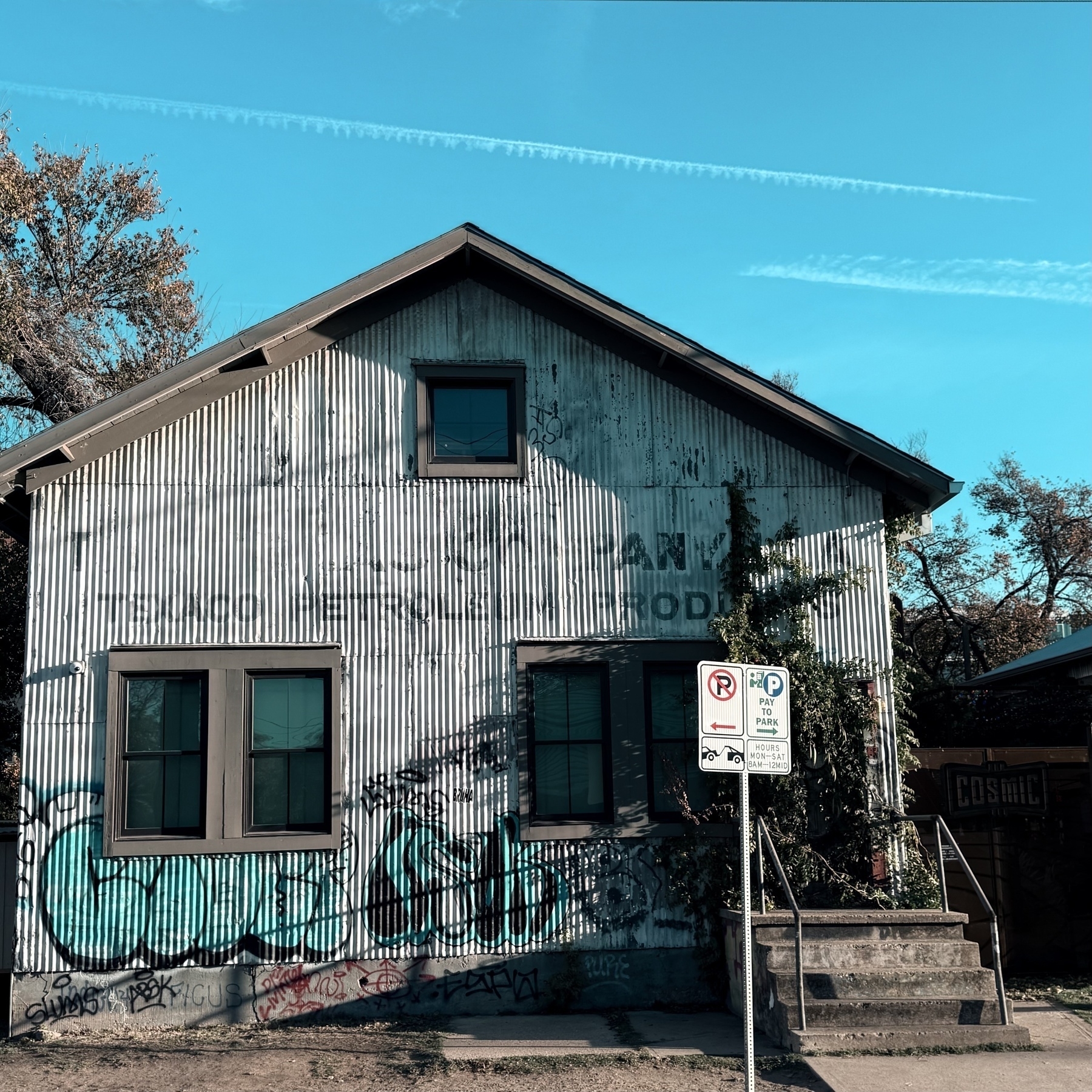 Building with windows and metal front with some graffiti and a no parking sign, blue sky in the background.