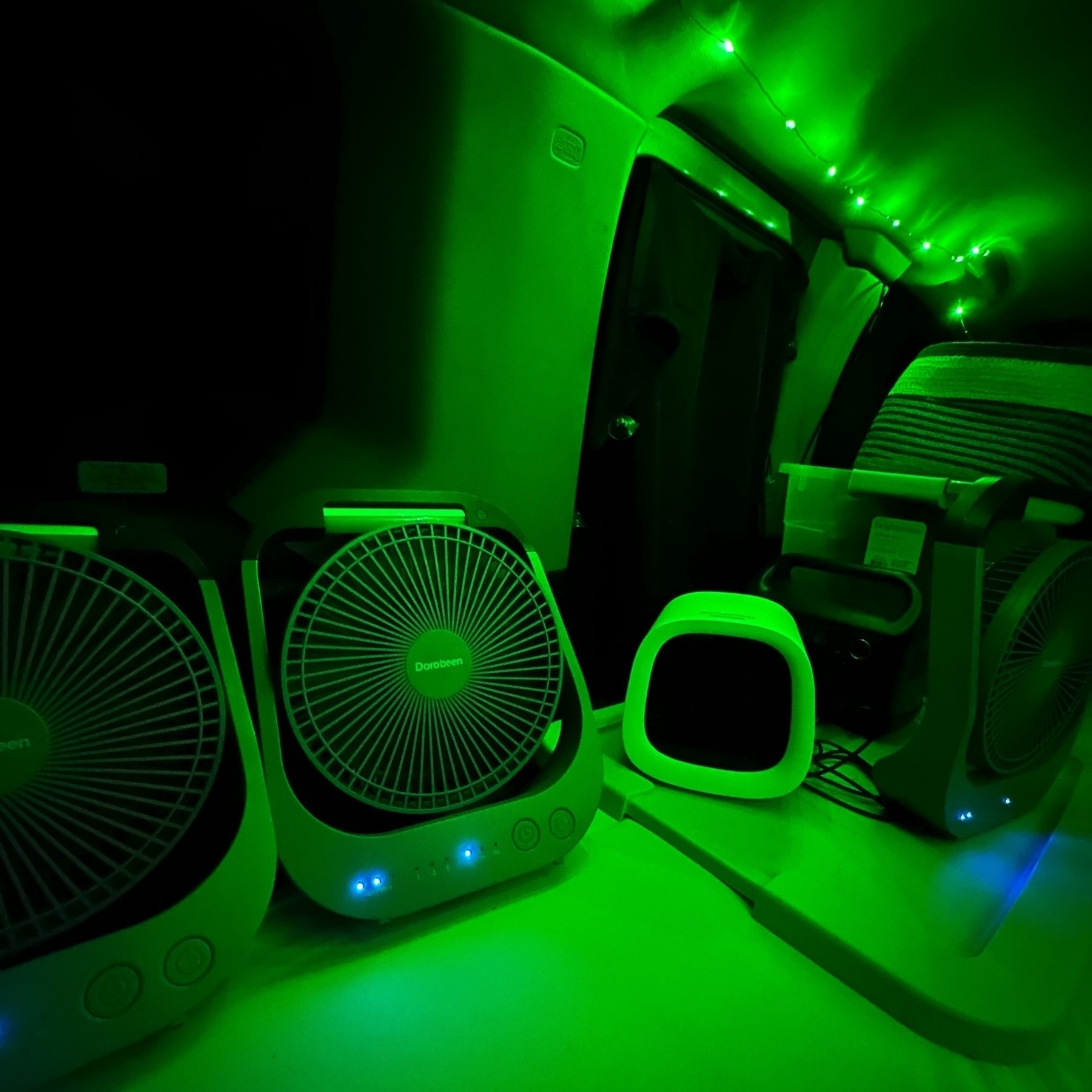 Inside my car at night, illuminated by green lights, with several fans and a battery lined up.