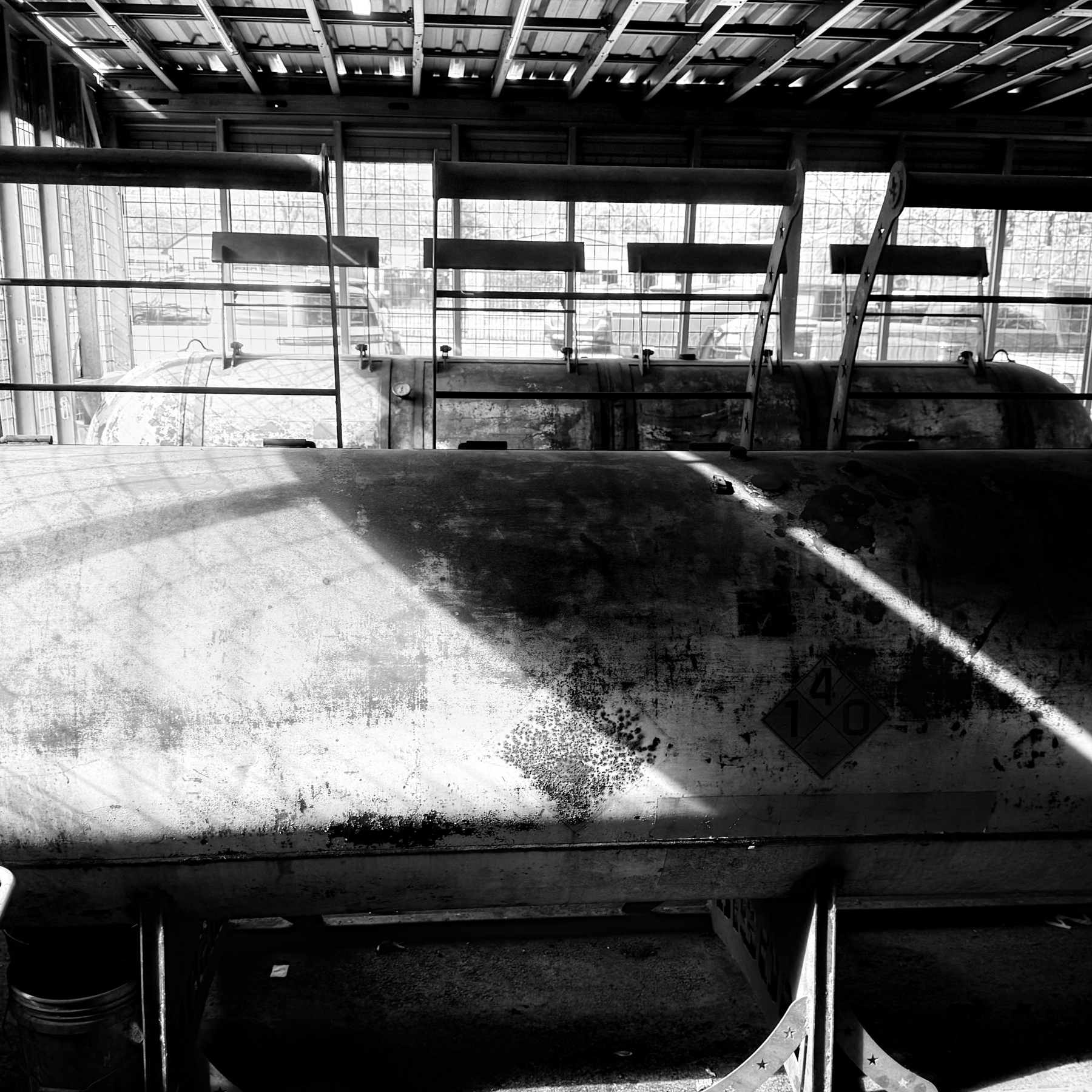 A black and white photograph features an industrial setting with large metal smokers inside a structure with a grid-like ceiling.