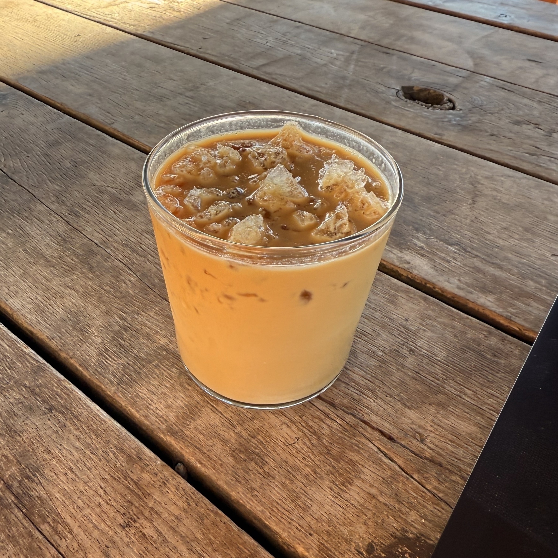 A glass of iced coffee sits on a wooden table.