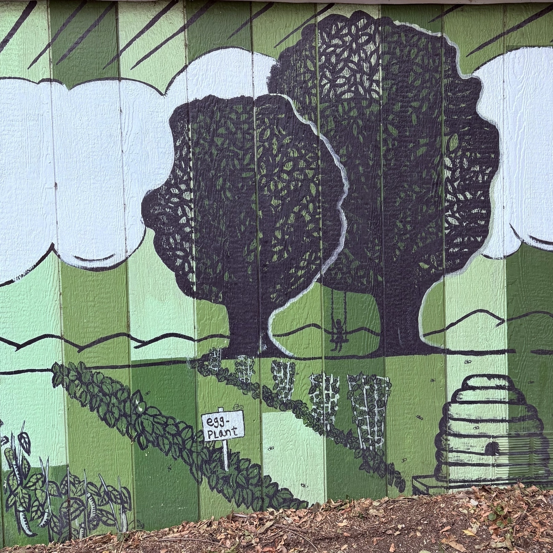 A green mural of a garden scene with trees, plants labeled eggplant, and a beehive.