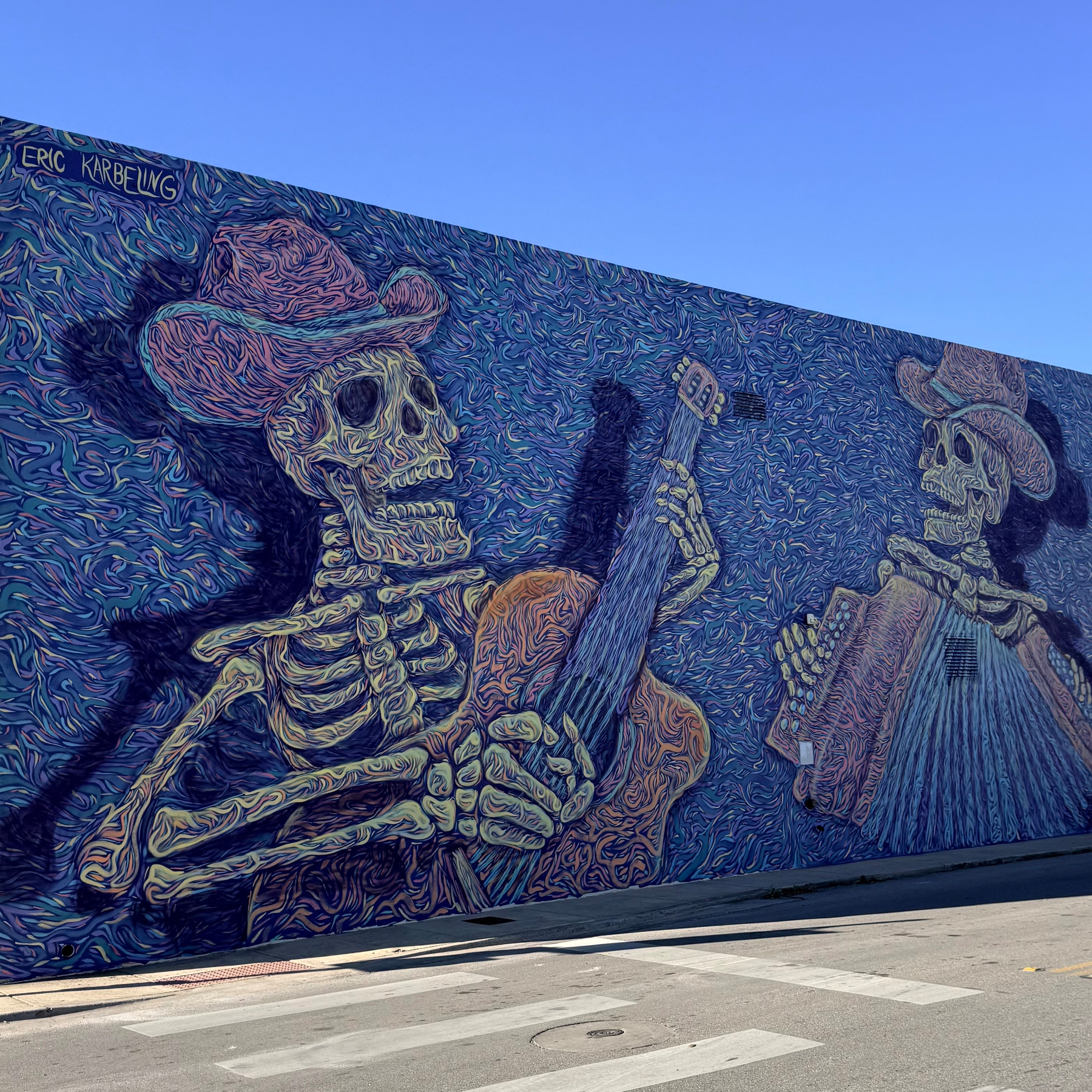 A vibrant mural depicts skeletons wearing hats and playing musical instruments against a swirling blue background.