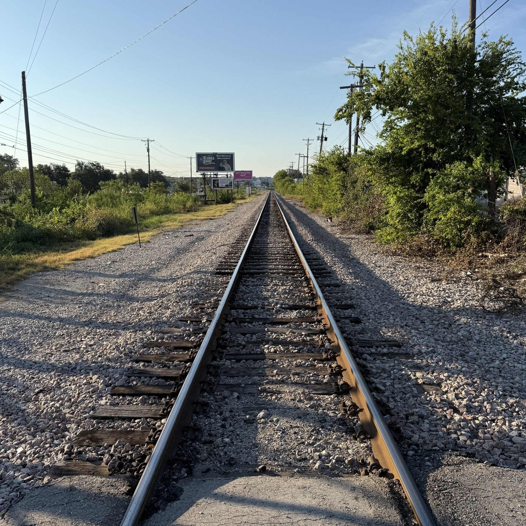 Railroad tracks stretch into the distance, flanked by greenery and utility poles, under a clear blue sky.