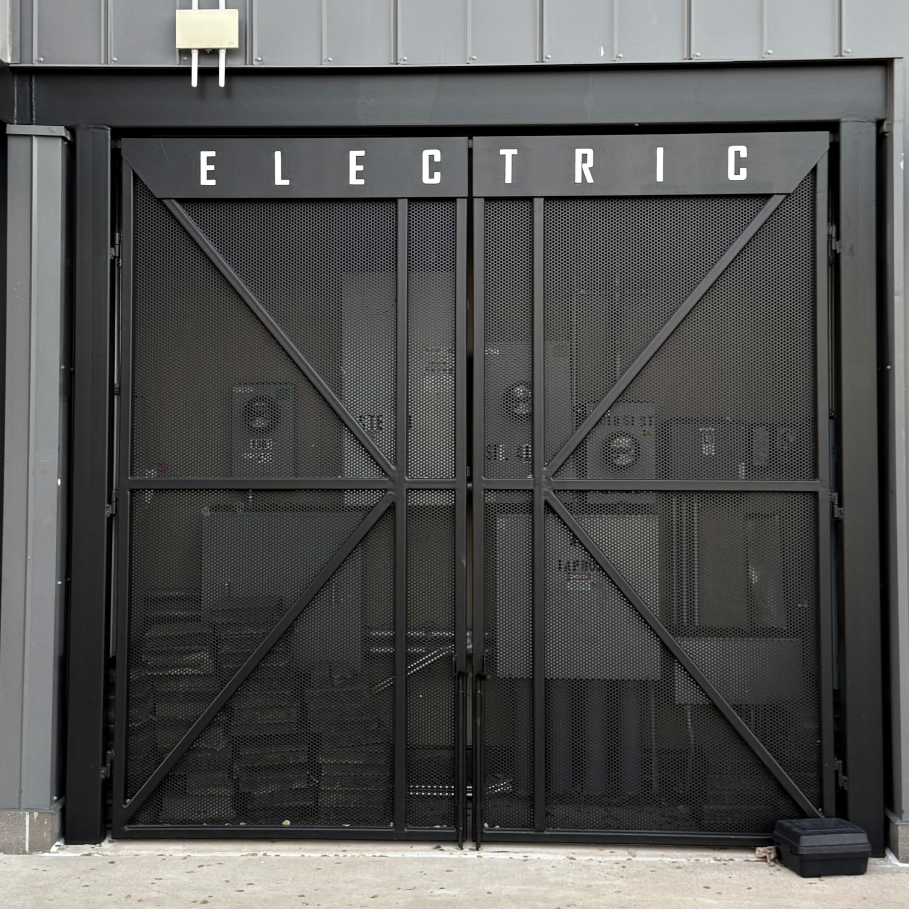A black metal gate labeled ELECTRIC covers electrical equipment against a gray building exterior.