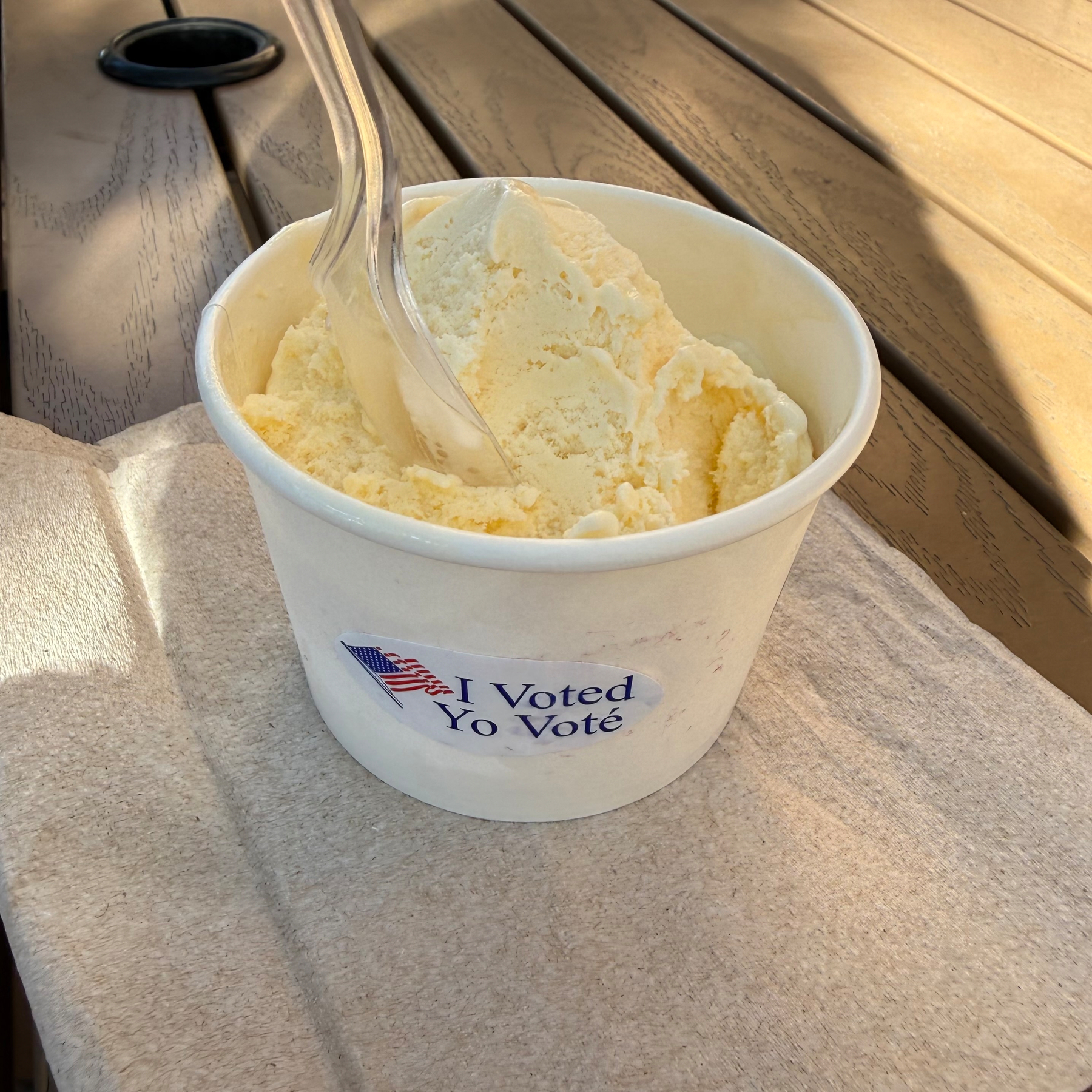 A cup of vanilla ice cream with a plastic spoon and a sticker that reads, I Voted Yo Voté.