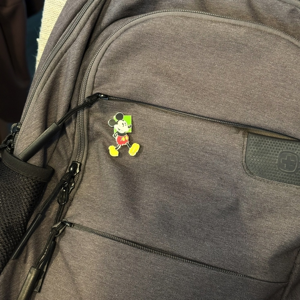 A gray backpack with a small pin featuring Mickey Mouse.