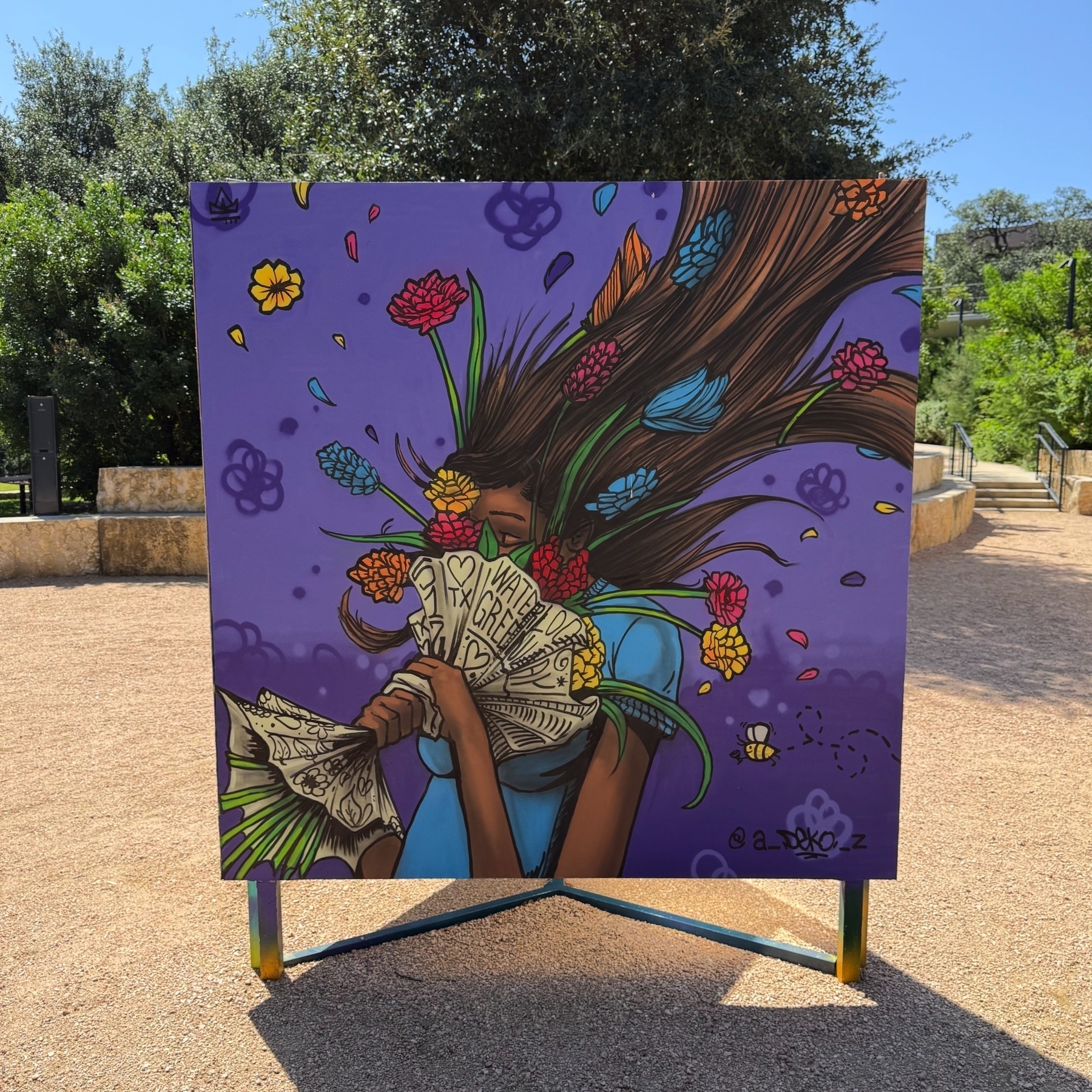 A colorful mural depicts a person with flowers wrapped in paper and flying up, set against a vibrant purple background.
