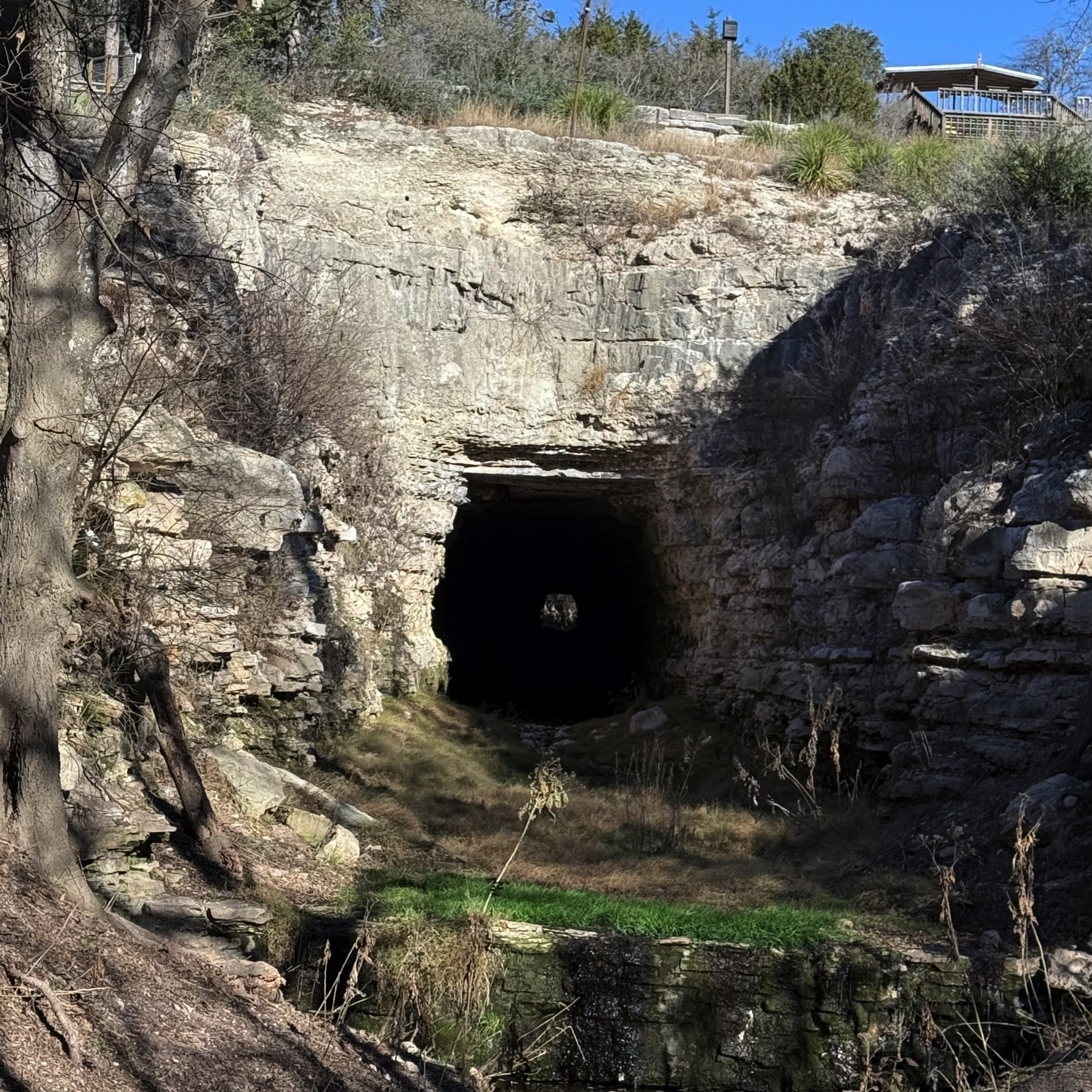 A tunnel entrance is set within a rocky hillside, surrounded by vegetation.