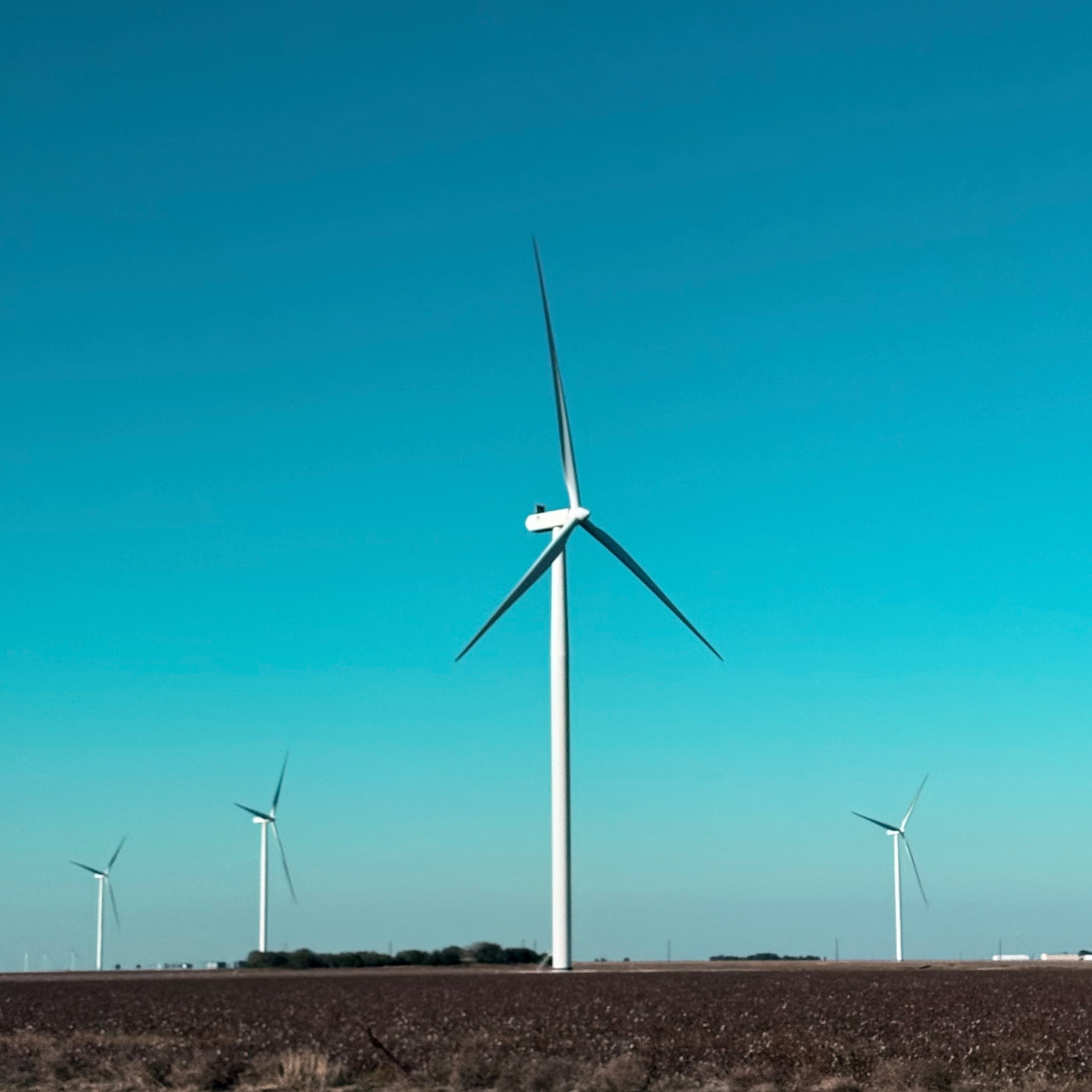 Wind turbines stand prominently in a field under a clear blue sky.