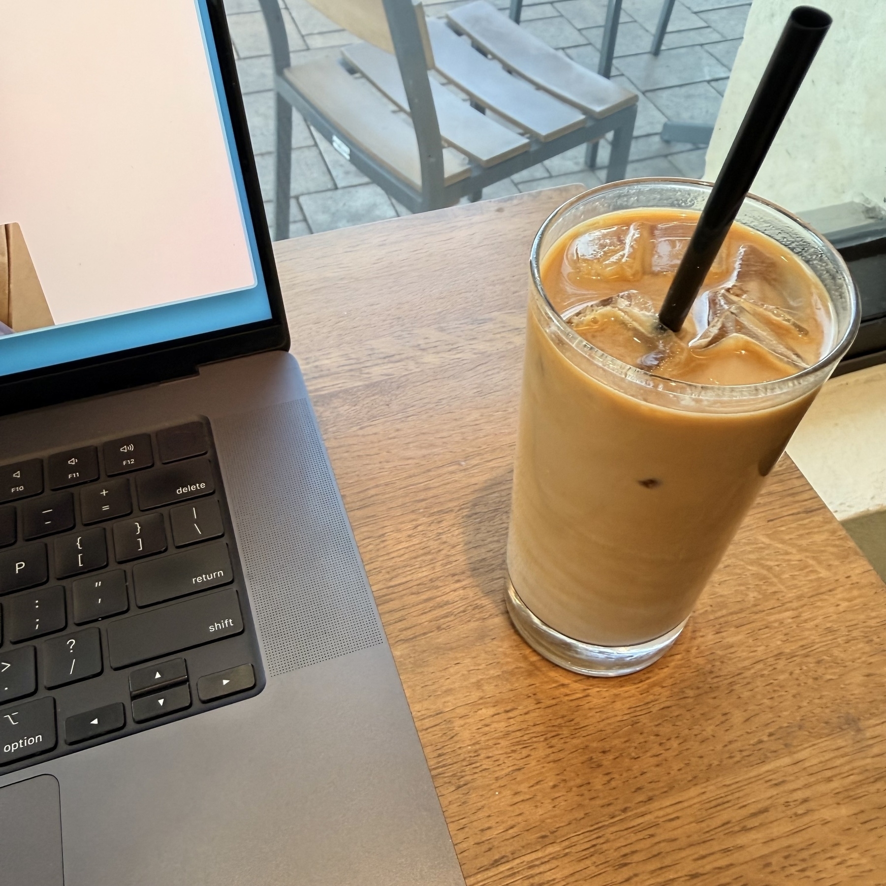 Iced latte in glass next to a laptop with just part of the screen visible.