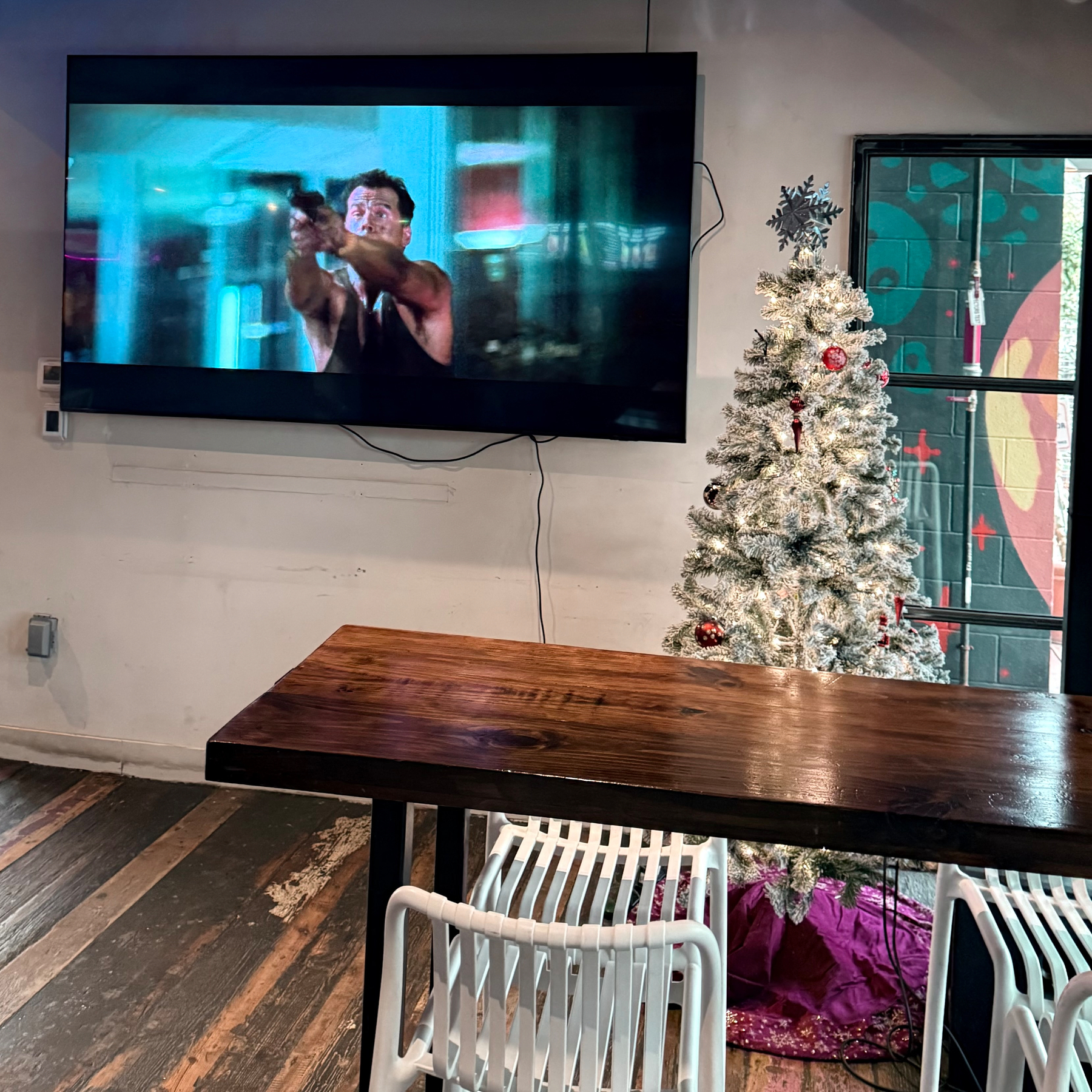TV displays an action movie scene above a wooden table and chairs next to a decorated Christmas tree.