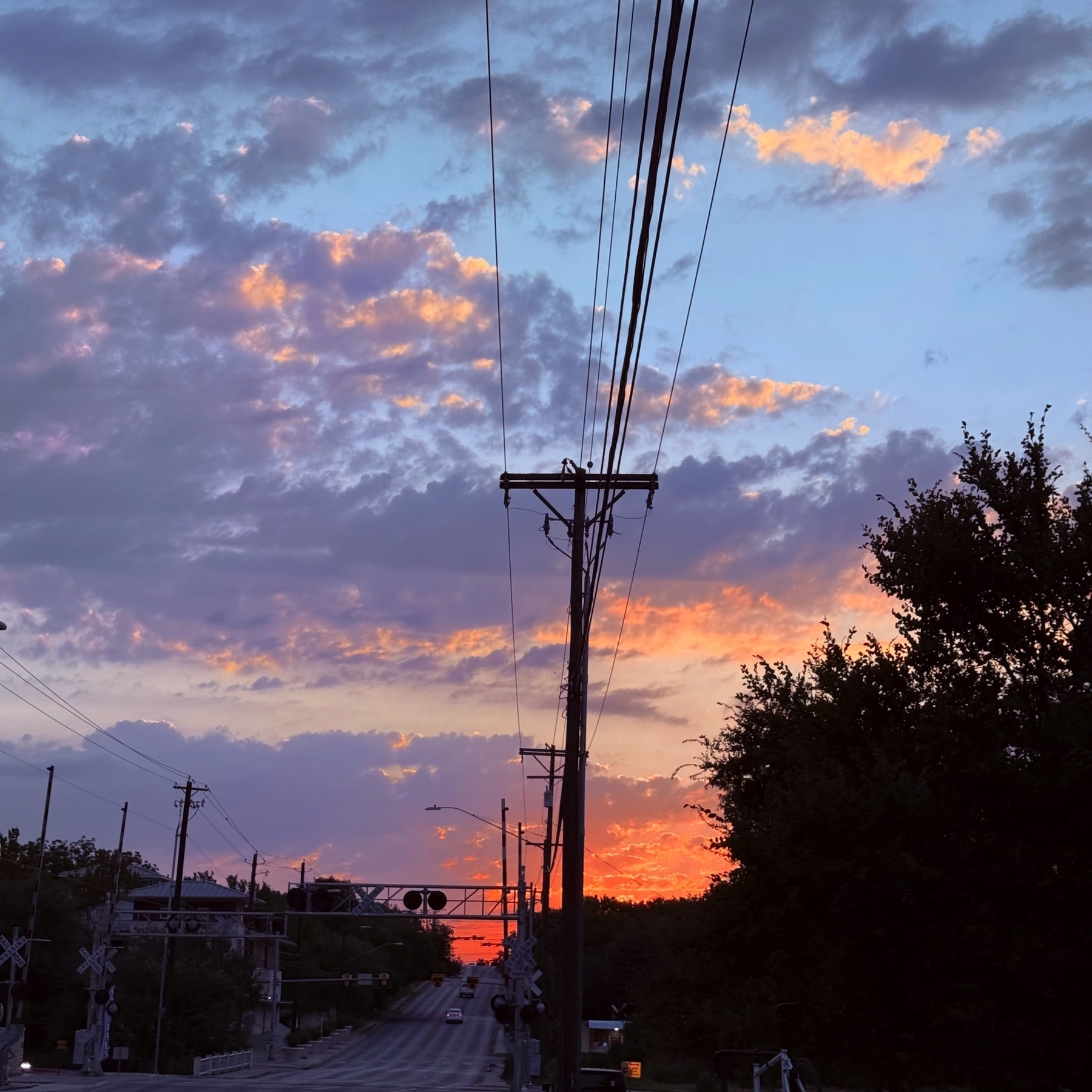 A scenic view of a sunrise sky with scattered clouds is visible above a road lined with power lines and trees.