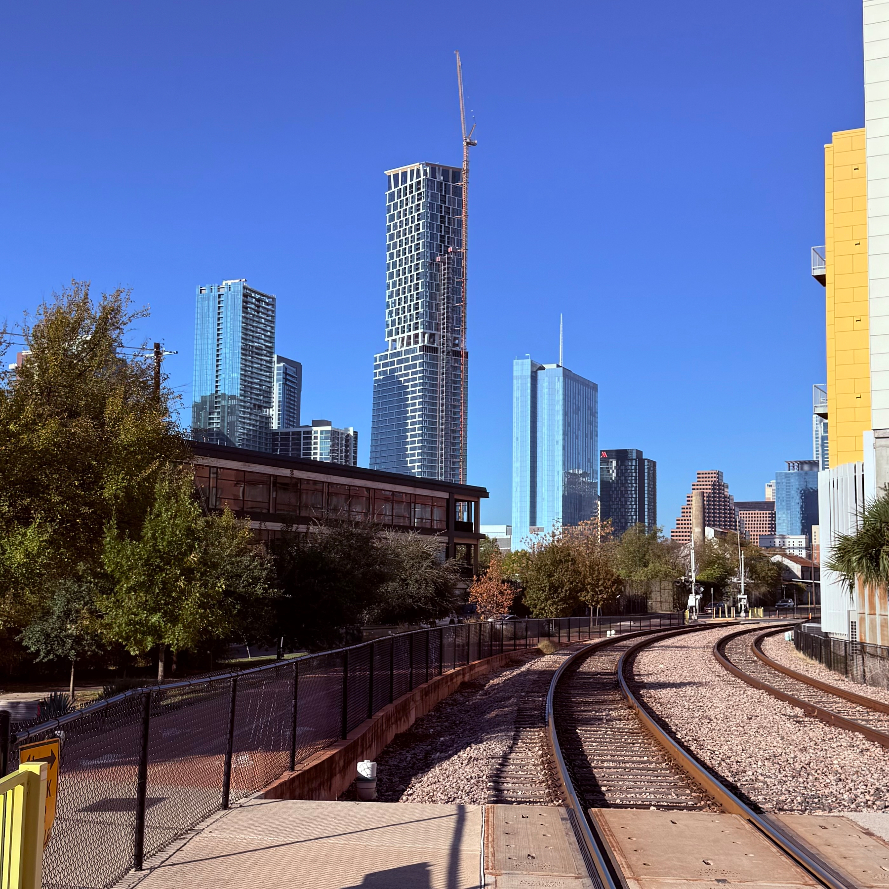 A railway track curves through a modern urban landscape with tall skyscrapers and trees lining the path.