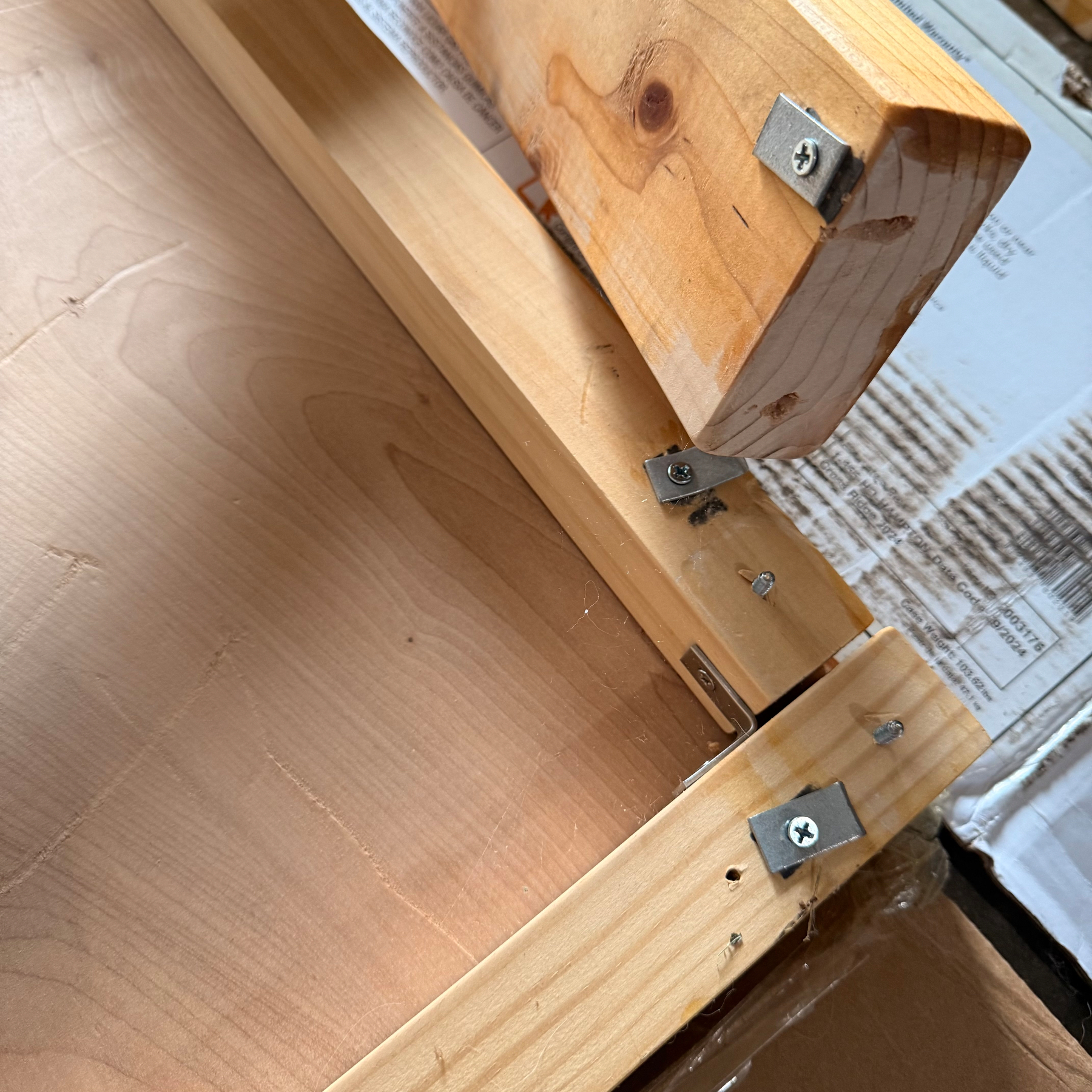 Wooden pieces are connected with metal brackets and screws, forming part of a bed frame.