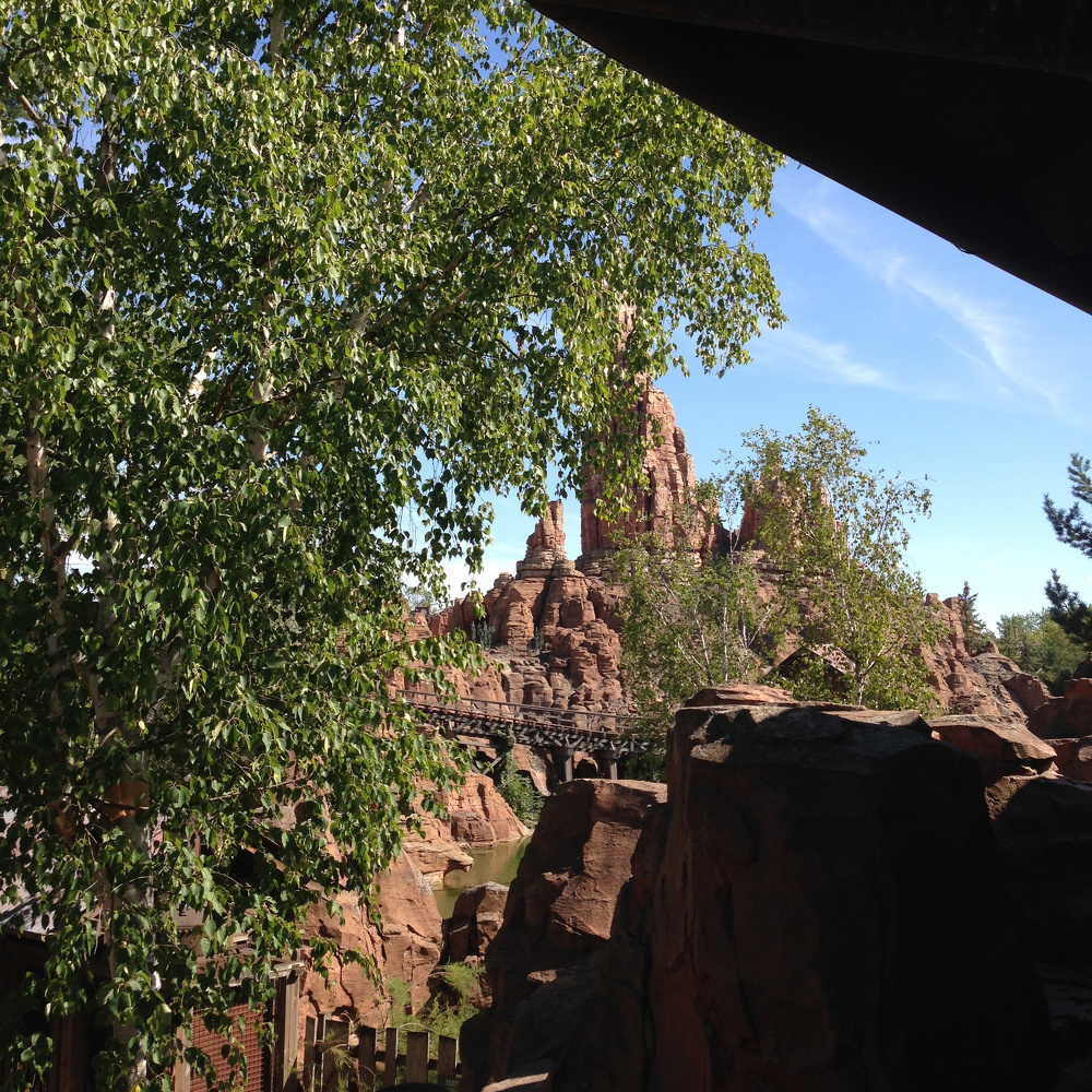 A rocky landscape features rugged cliffs and lush trees under a clear blue sky.