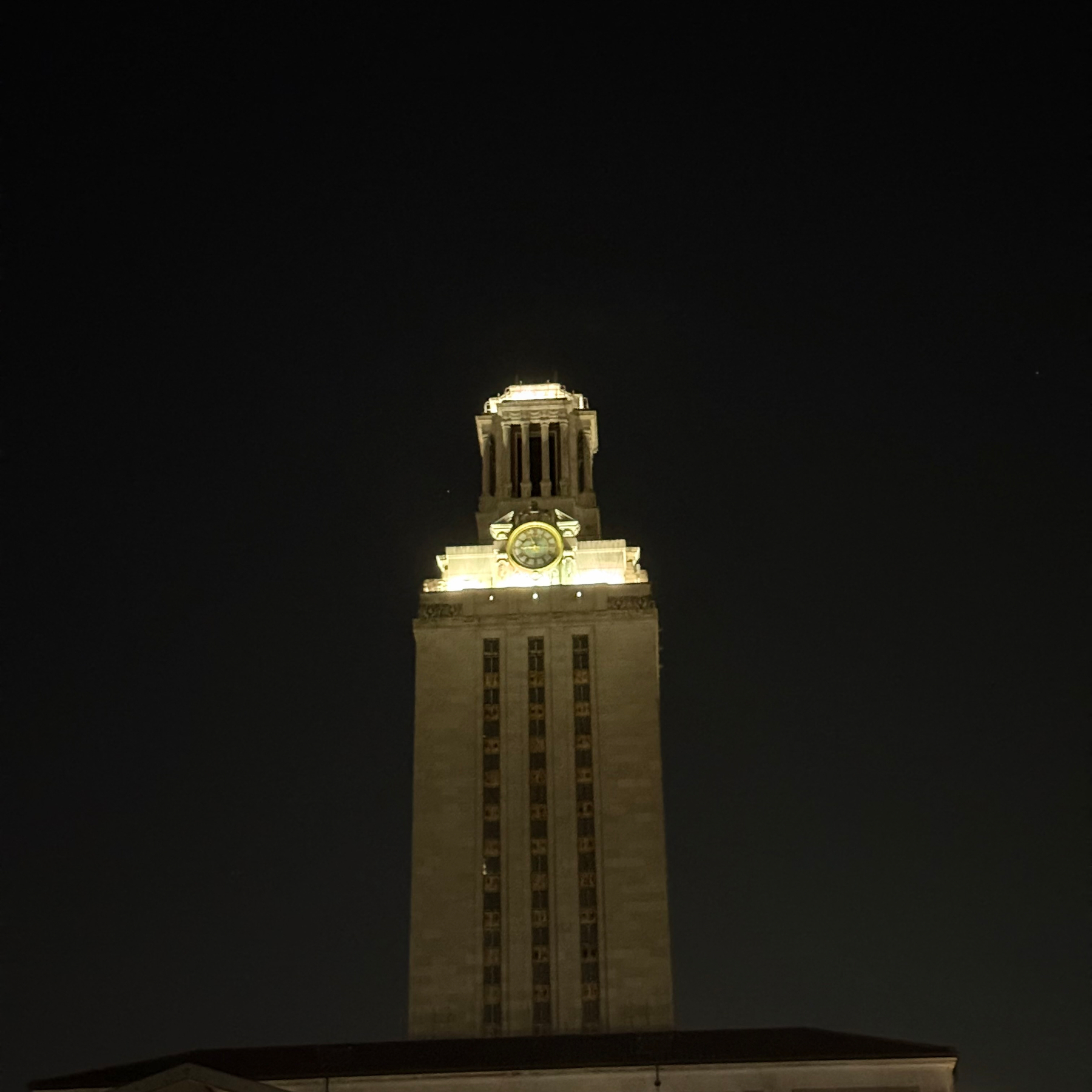 A tall clock tower brightly illuminated at night against a dark sky.