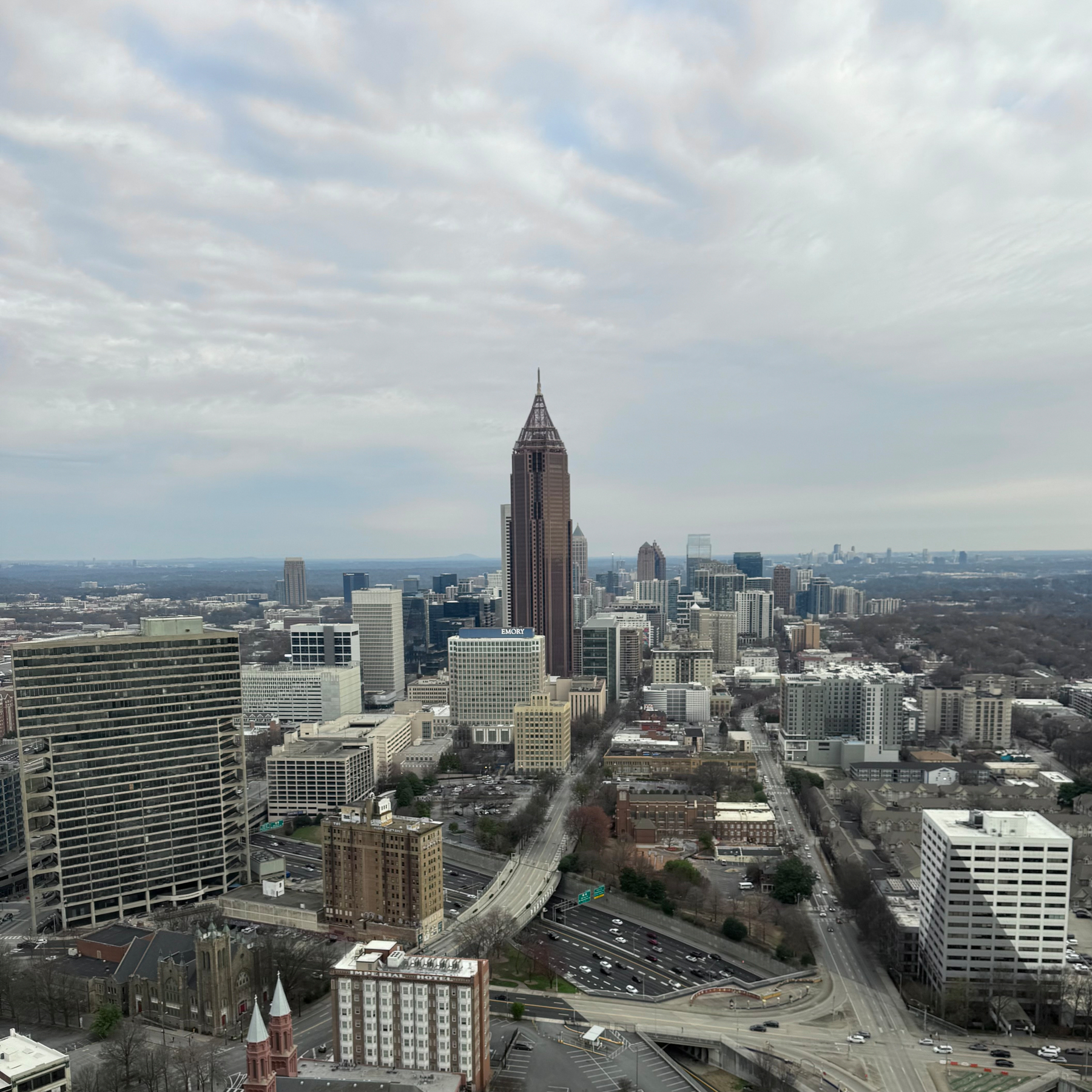 A sprawling cityscape features numerous high-rise buildings under a cloudy sky.