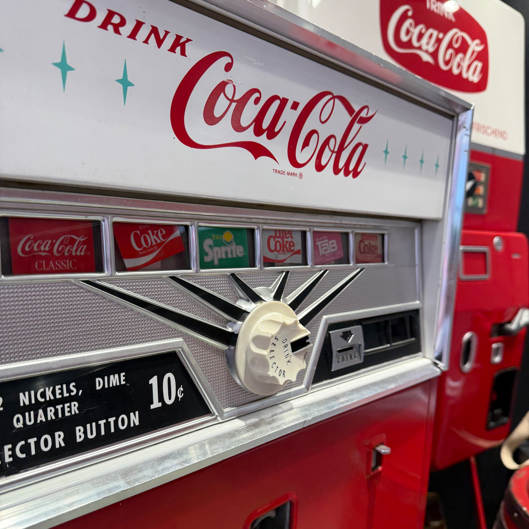A vintage Coca-Cola vending machine features classic branding and a mechanical coin slot.