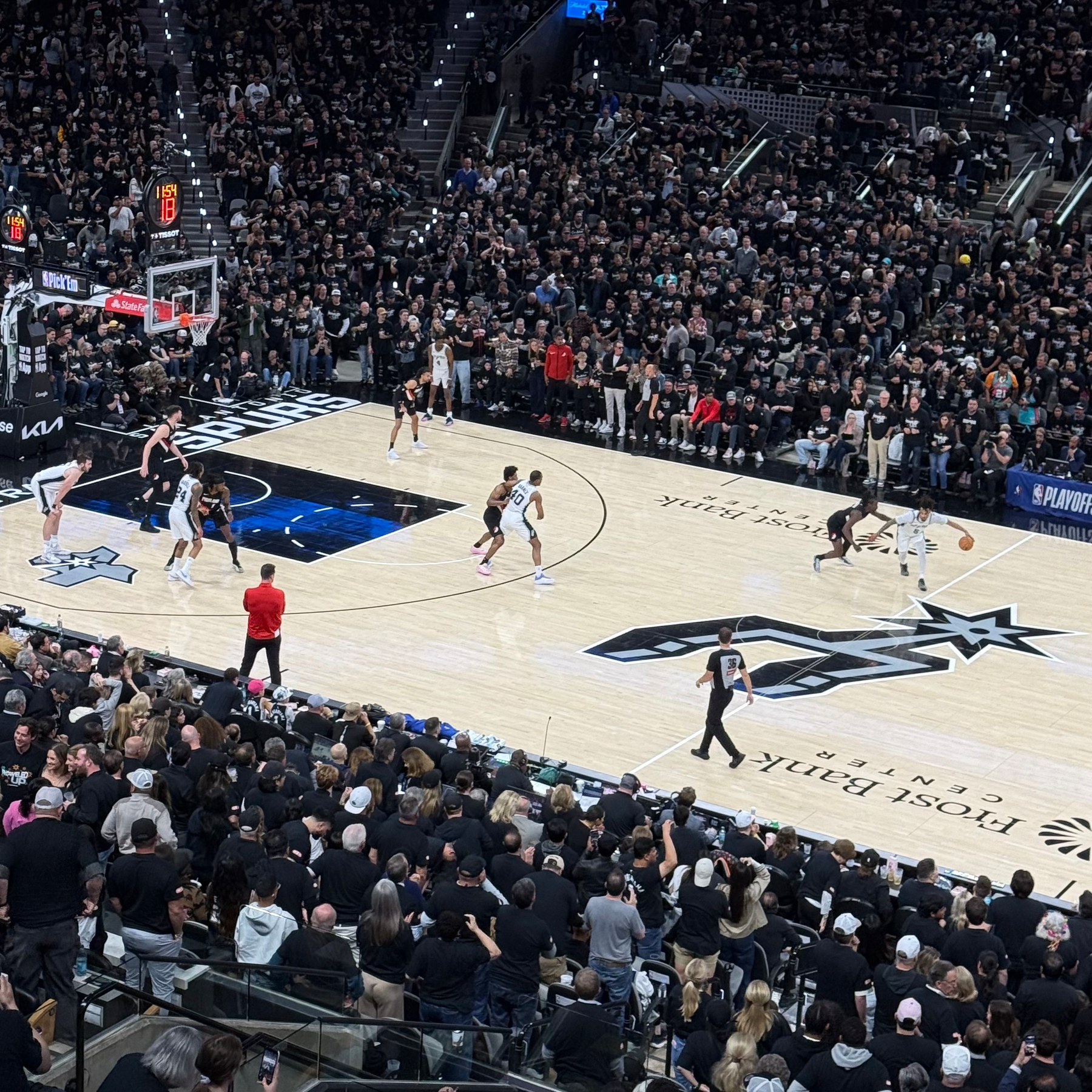 A basketball game is taking place in a packed arena with one team on offense near the three-point line.