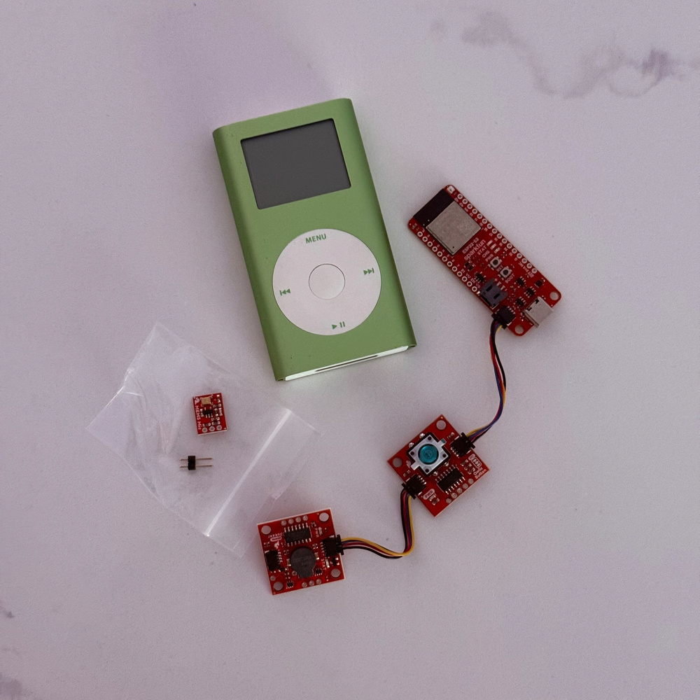 A green iPod Mini is placed next to several small red electronic circuit boards connected by wires on a white surface.