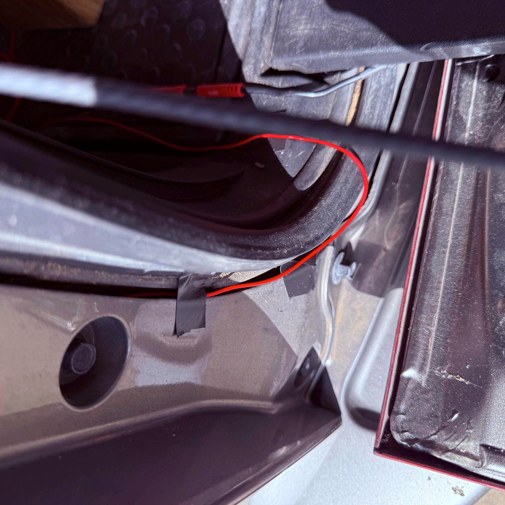 A red wire is taped along the edge of a car door frame, with the door partially open.