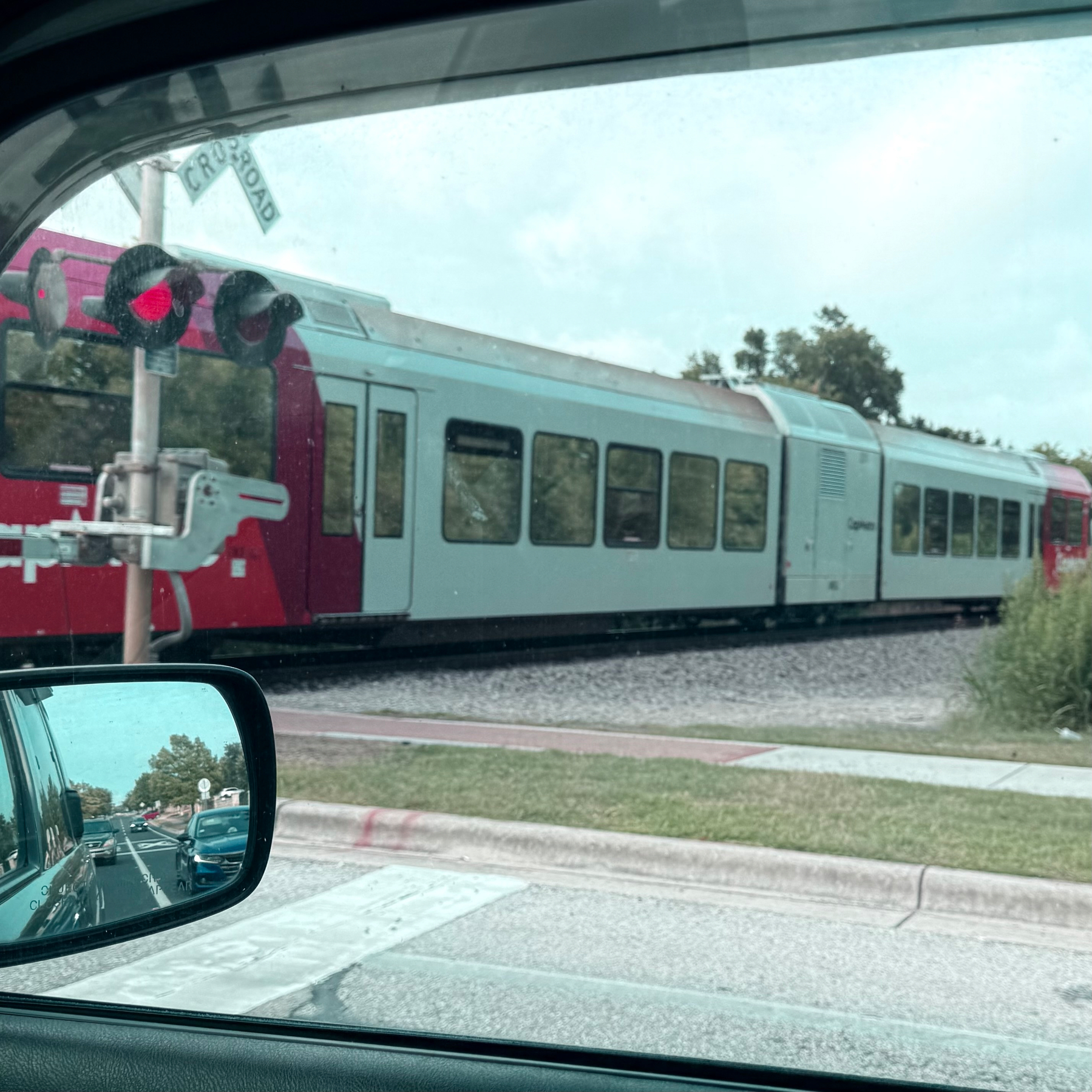 A train is passing by a railroad crossing while a car waits at an intersection, visible through the side mirror.