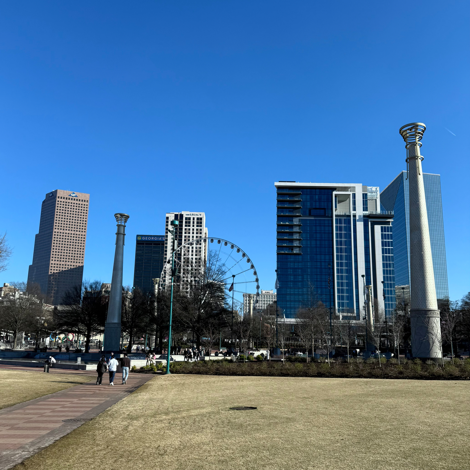 Atlanta cityscape features a Ferris wheel, modern skyscrapers, and two large columns against a clear blue sky.