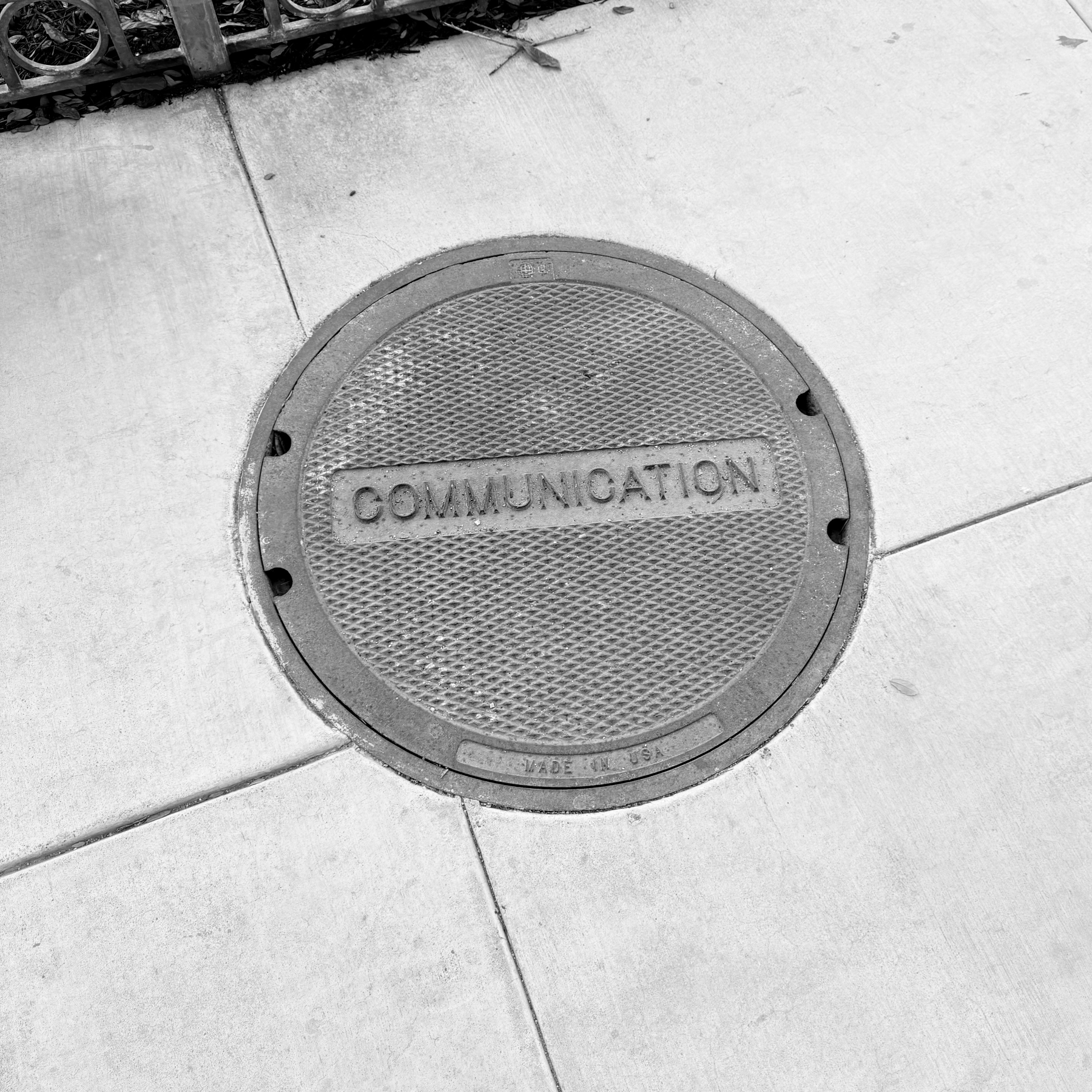 A circular manhole cover embedded in a sidewalk displays the word COMMUNICATION.