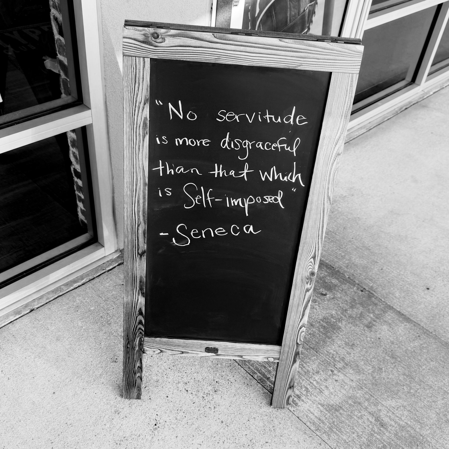 A blackboard sign outside a building displays a quote by Seneca: No servitude is more disgraceful than that which is self-imposed.