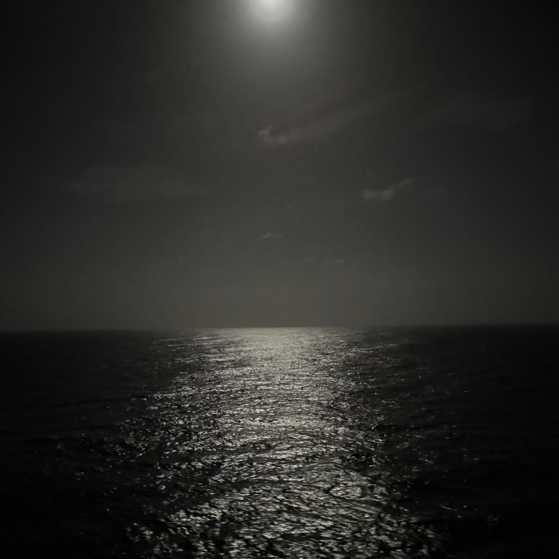 A moonlit night sky casts a serene glow over a tranquil ocean.