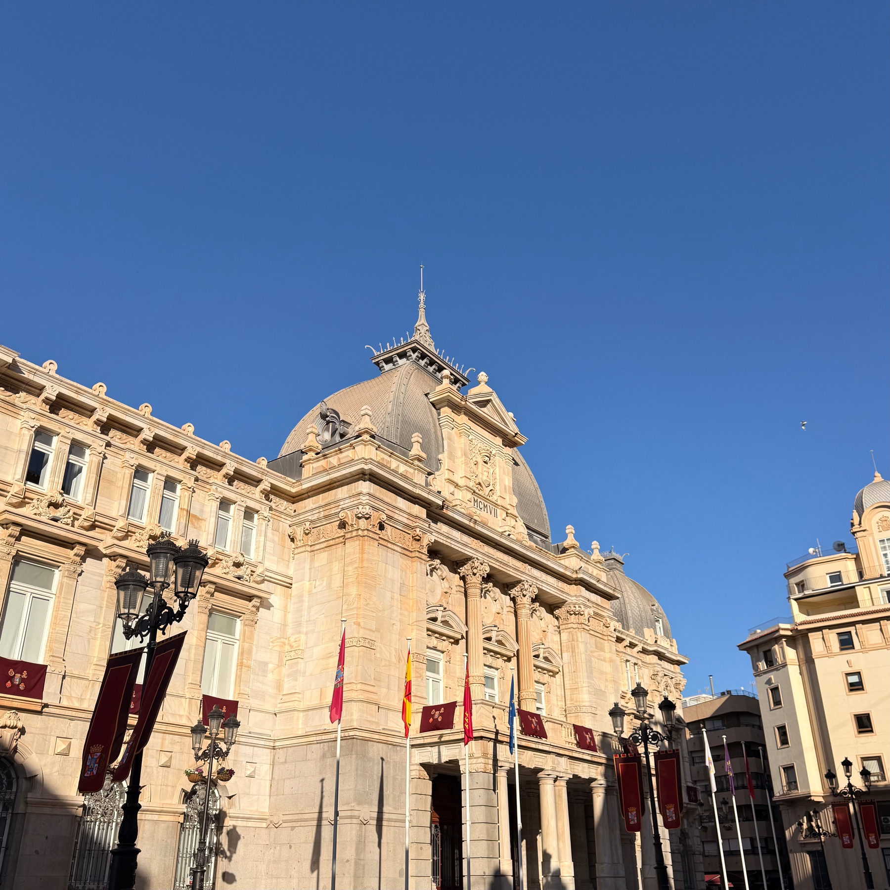 A historic building with a domed roof is adorned with flags and banners under a clear blue sky.