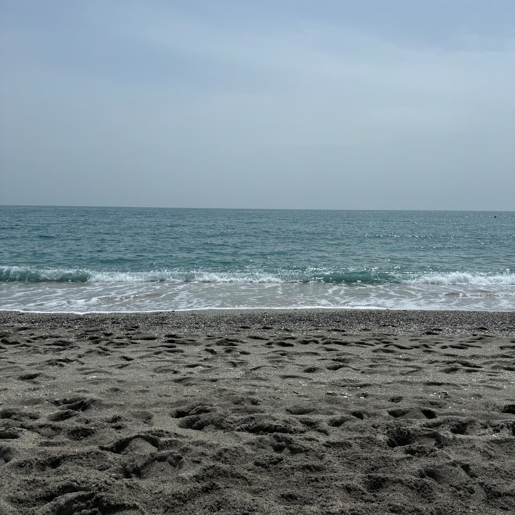 A tranquil beach scene features gentle waves lapping against the sandy shore under a cloudy sky.