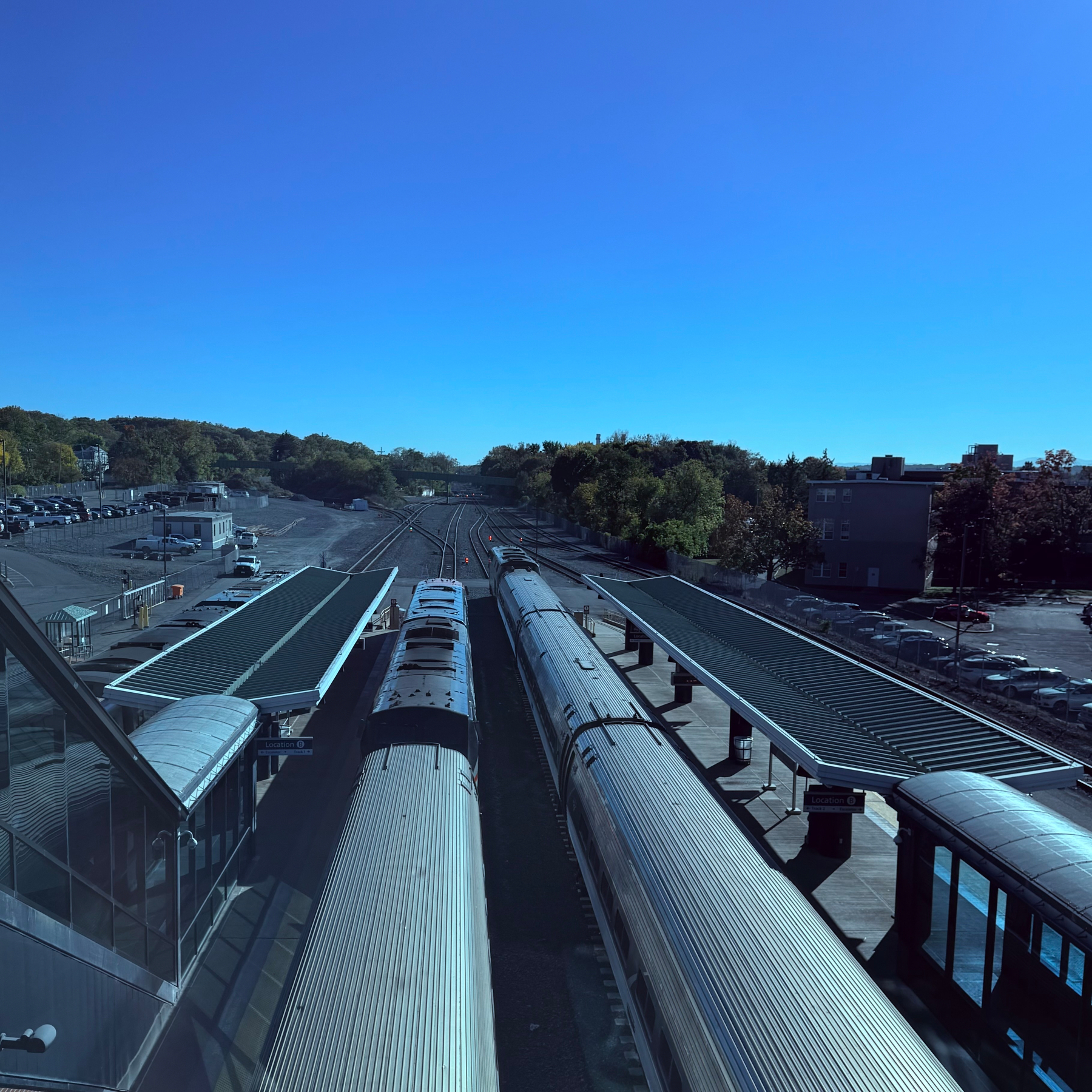 Two trains are parked at a railway station with platforms on either side under a clear blue sky.