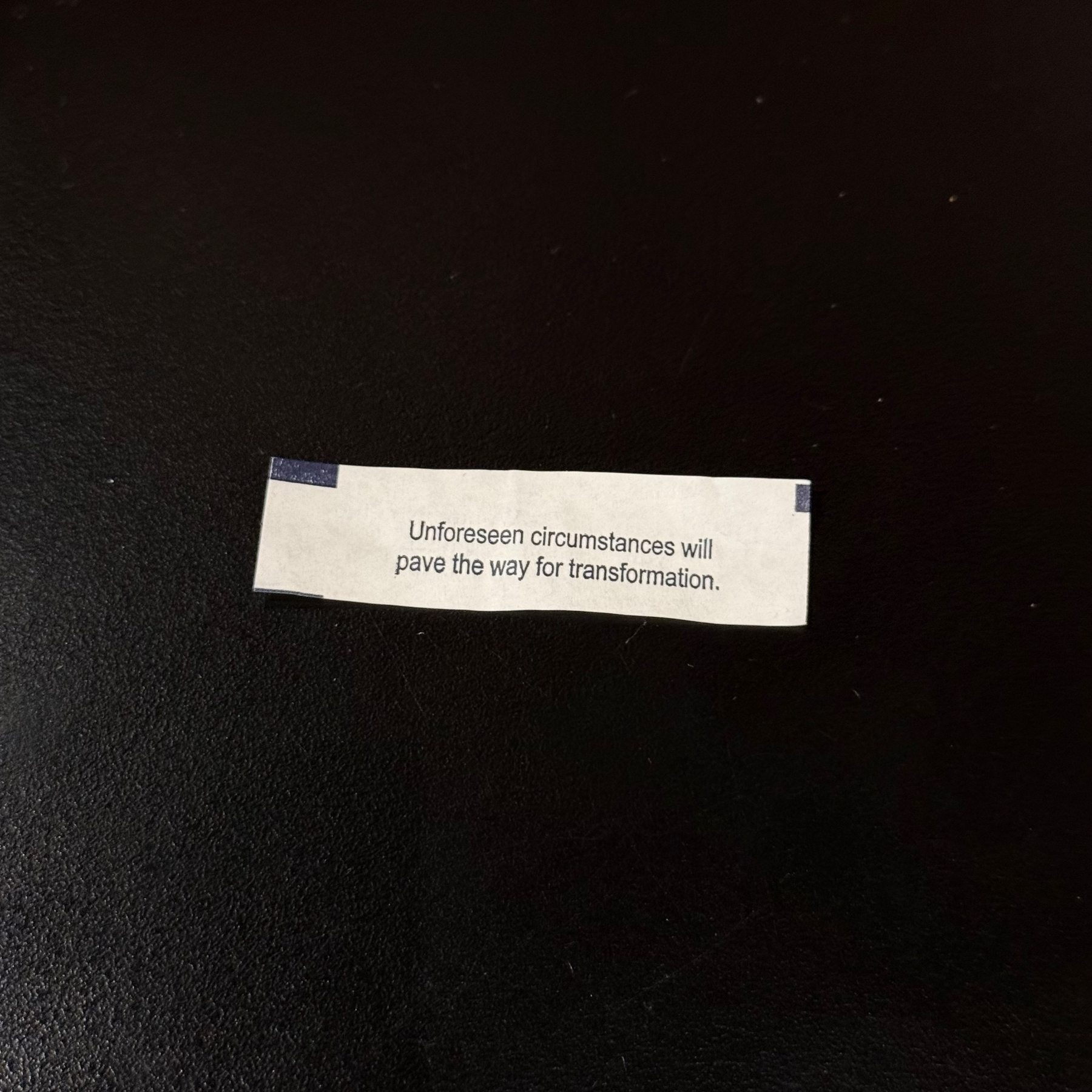 A fortune cookie slip on dark table with the message Unforeseen circumstances will pave the way for transformation.