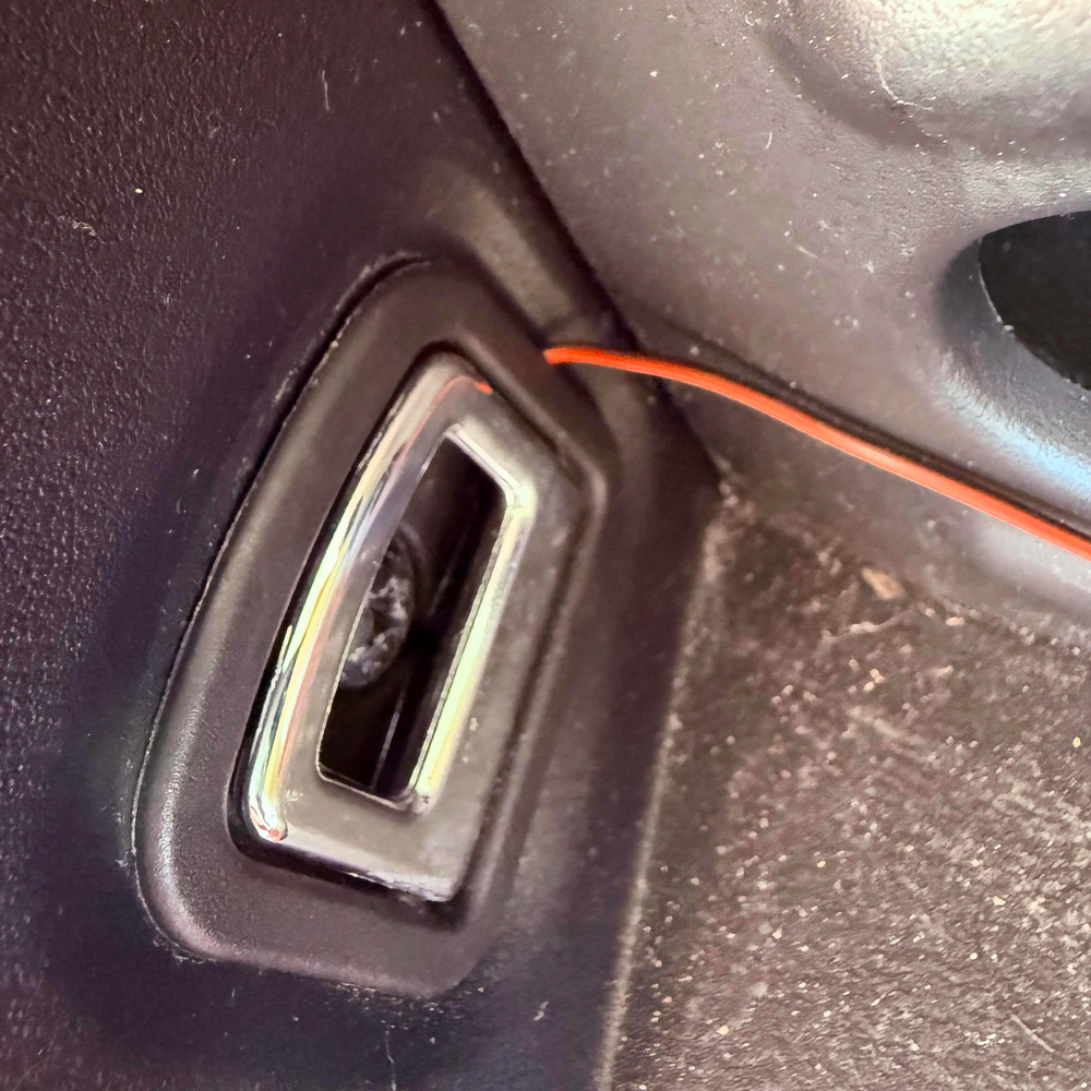 A close-up view of a car's interior showing a metallic door latch mechanism and a red wire running along the edge.