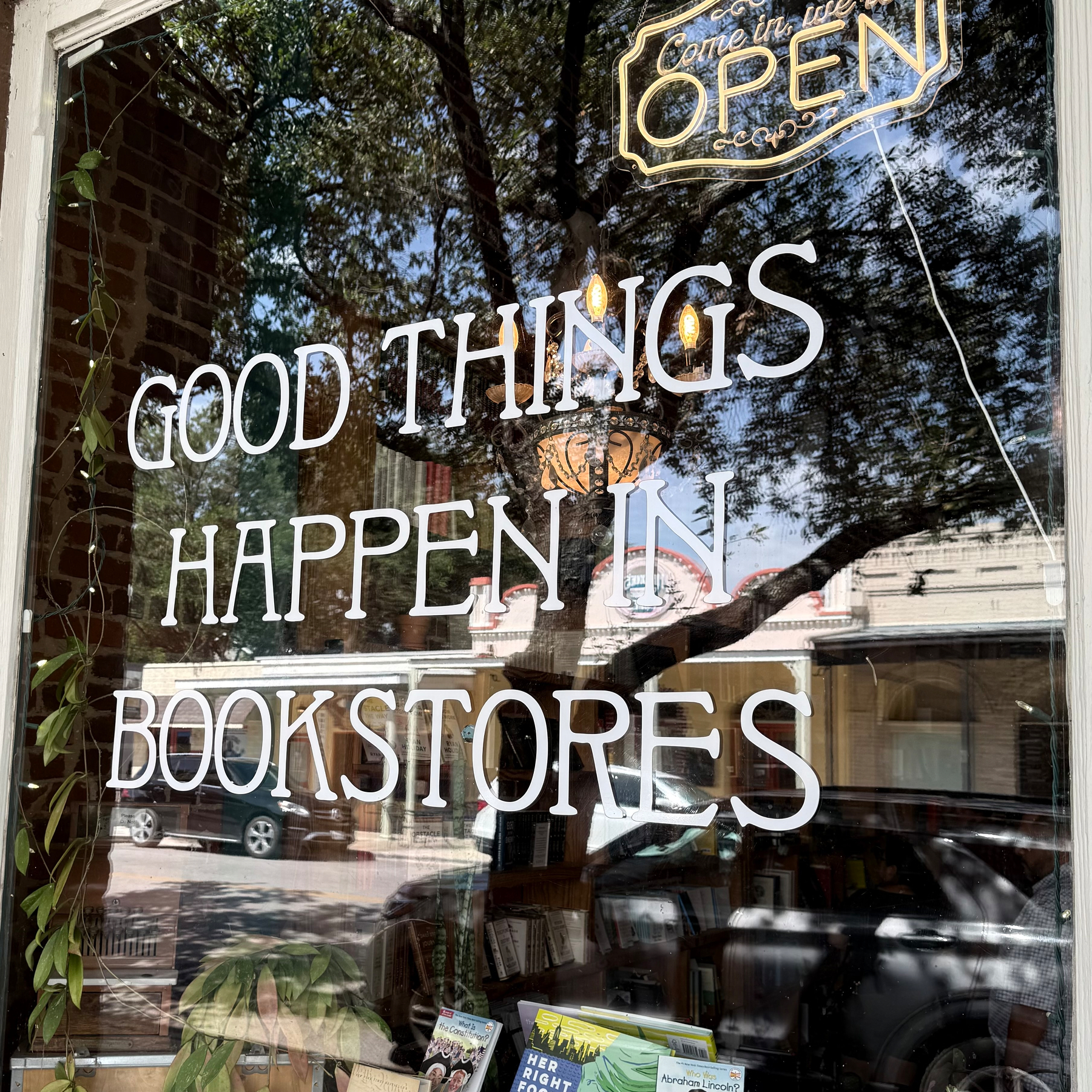 A bookstore window displays the phrase GOOD THINGS HAPPEN IN BOOKSTORES along with a neon OPEN sign.