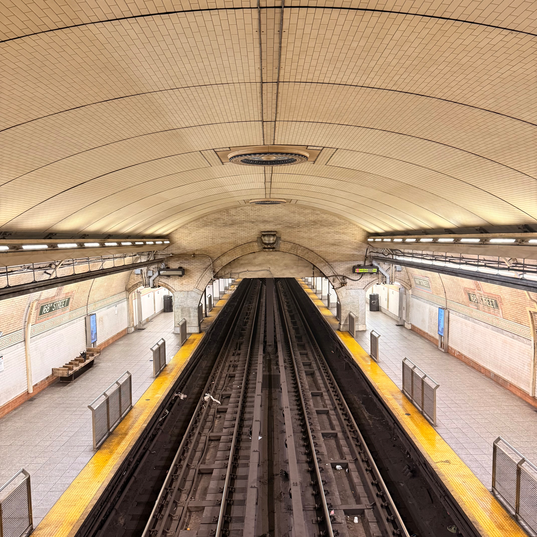 An empty subway station platform with two tracks running through the middle is shown from an elevated central viewpoint.