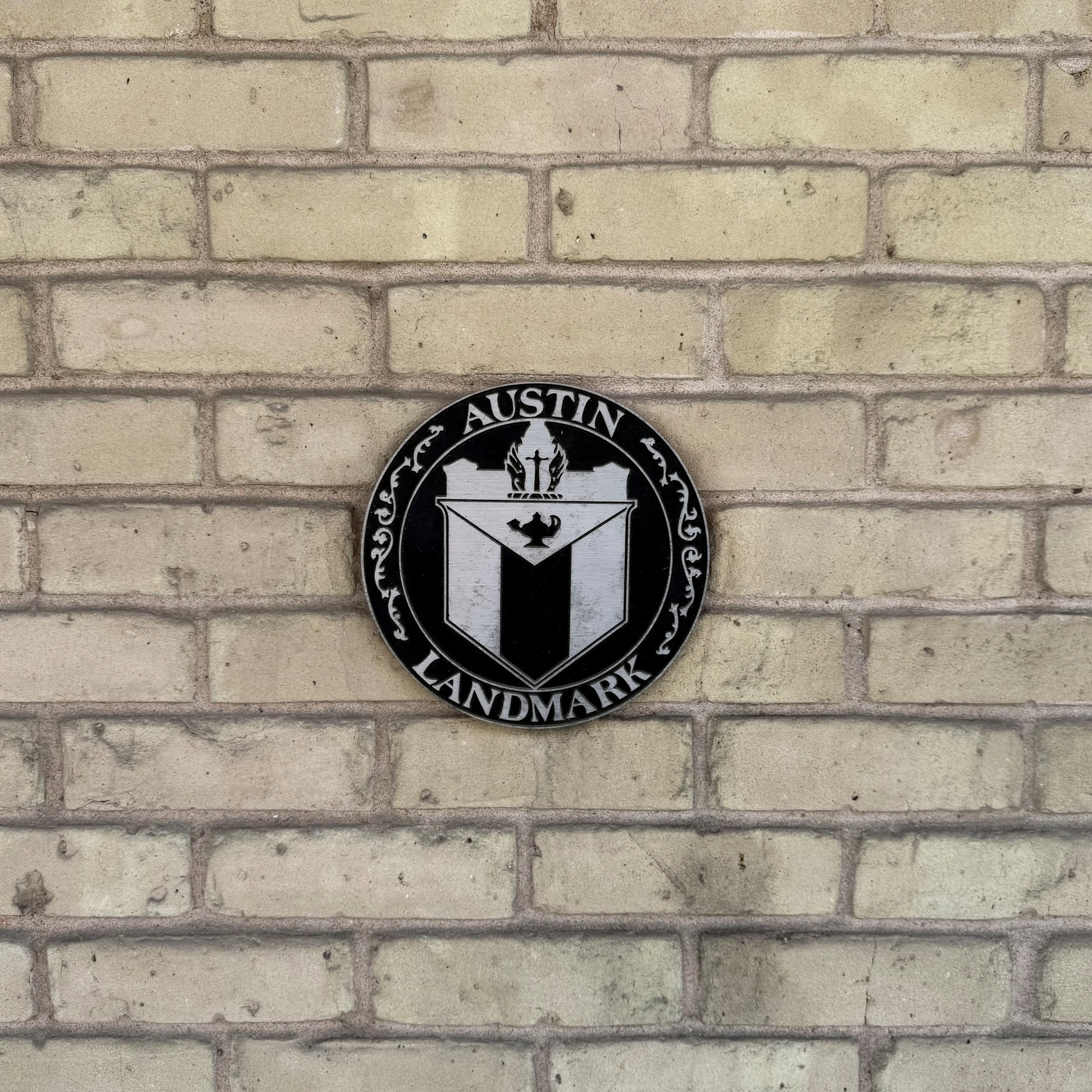 A circular plaque with the text Austin Landmark and a crest is mounted on a brick wall.