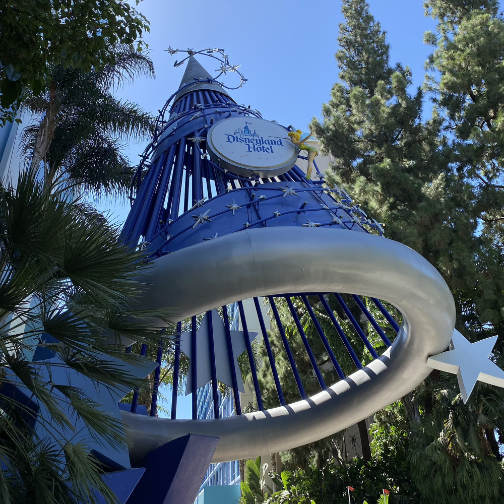 A large, blue sorcerer's hat structure with stars and a Disneyland Hotel sign is surrounded by tall trees.