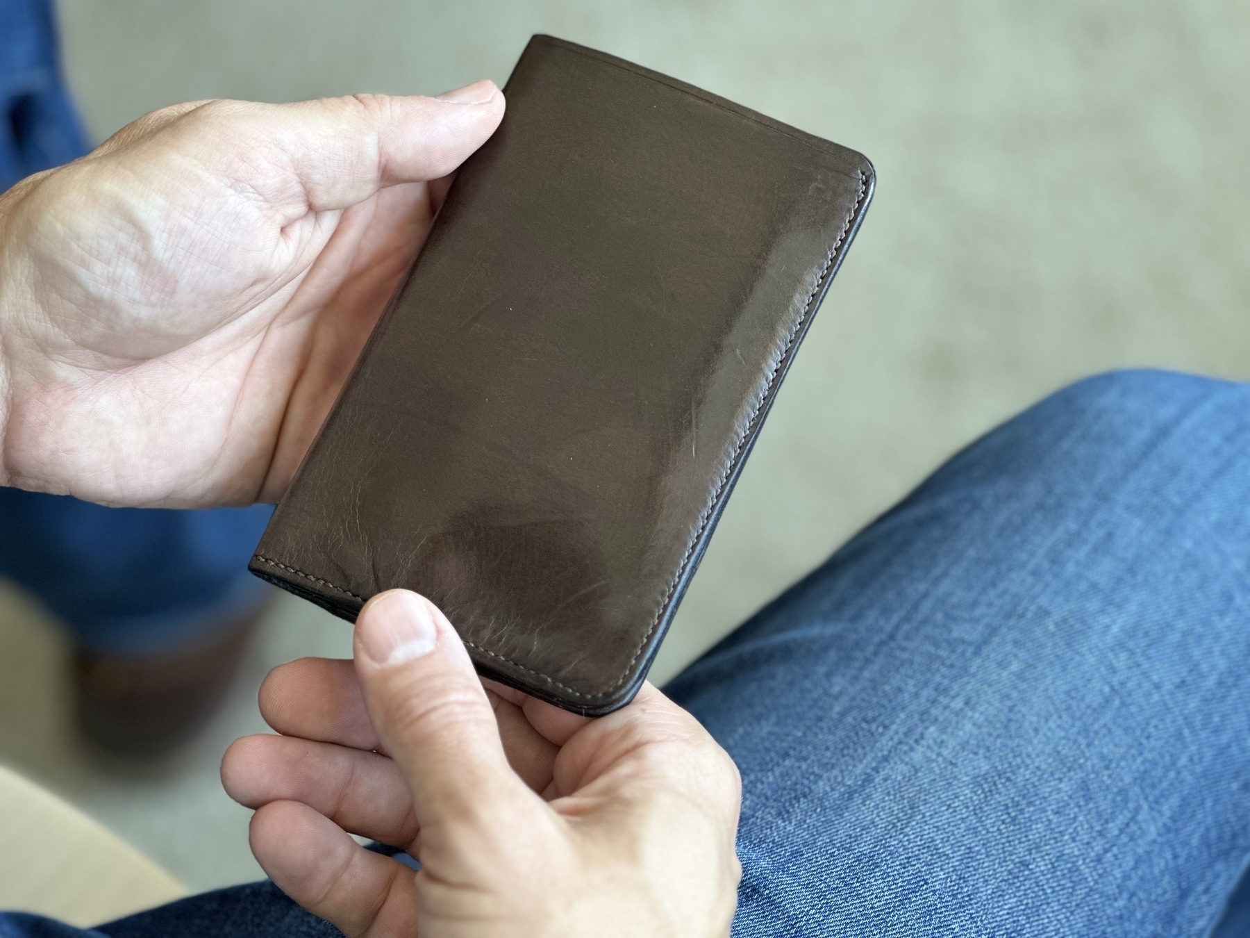 Chocolate brown leather wallet closed and held with two hands. 