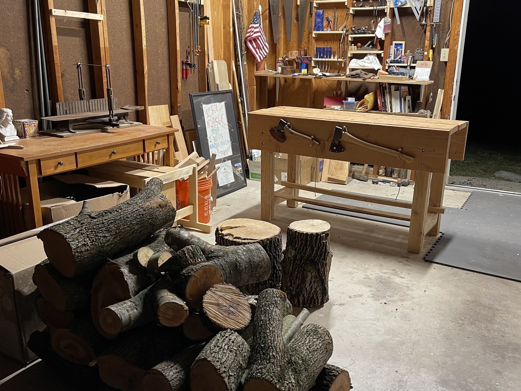 My previous workshop in December of 2020. My start in handcrafts. In what was then my garage. In view is a pile of cherry wood for use on future projects I had planned, my workbench, and my hand tools hanging on the far wall. 