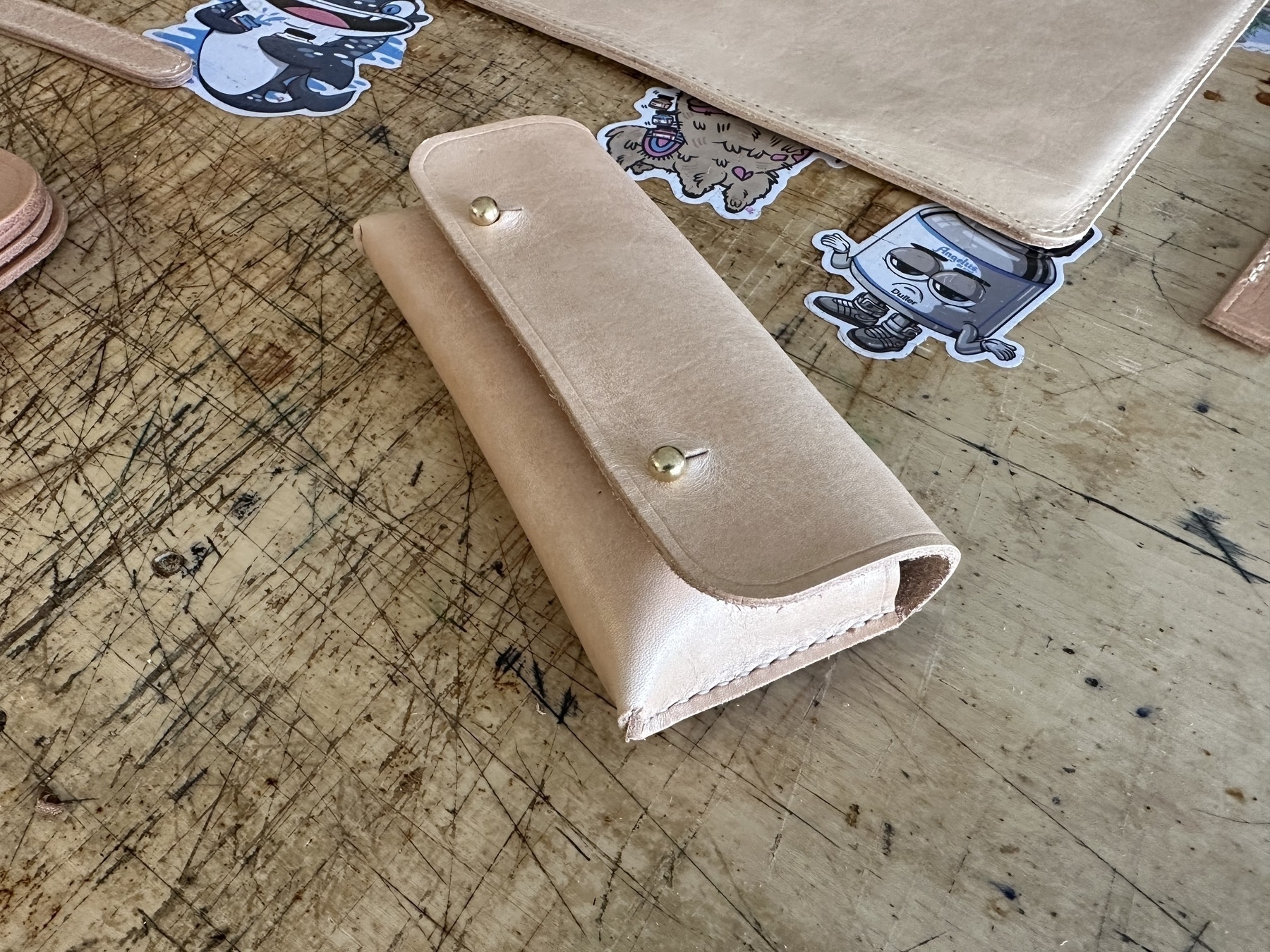 small undyed leather pouch laying on a table. External flap enclosed with two solid button studs.