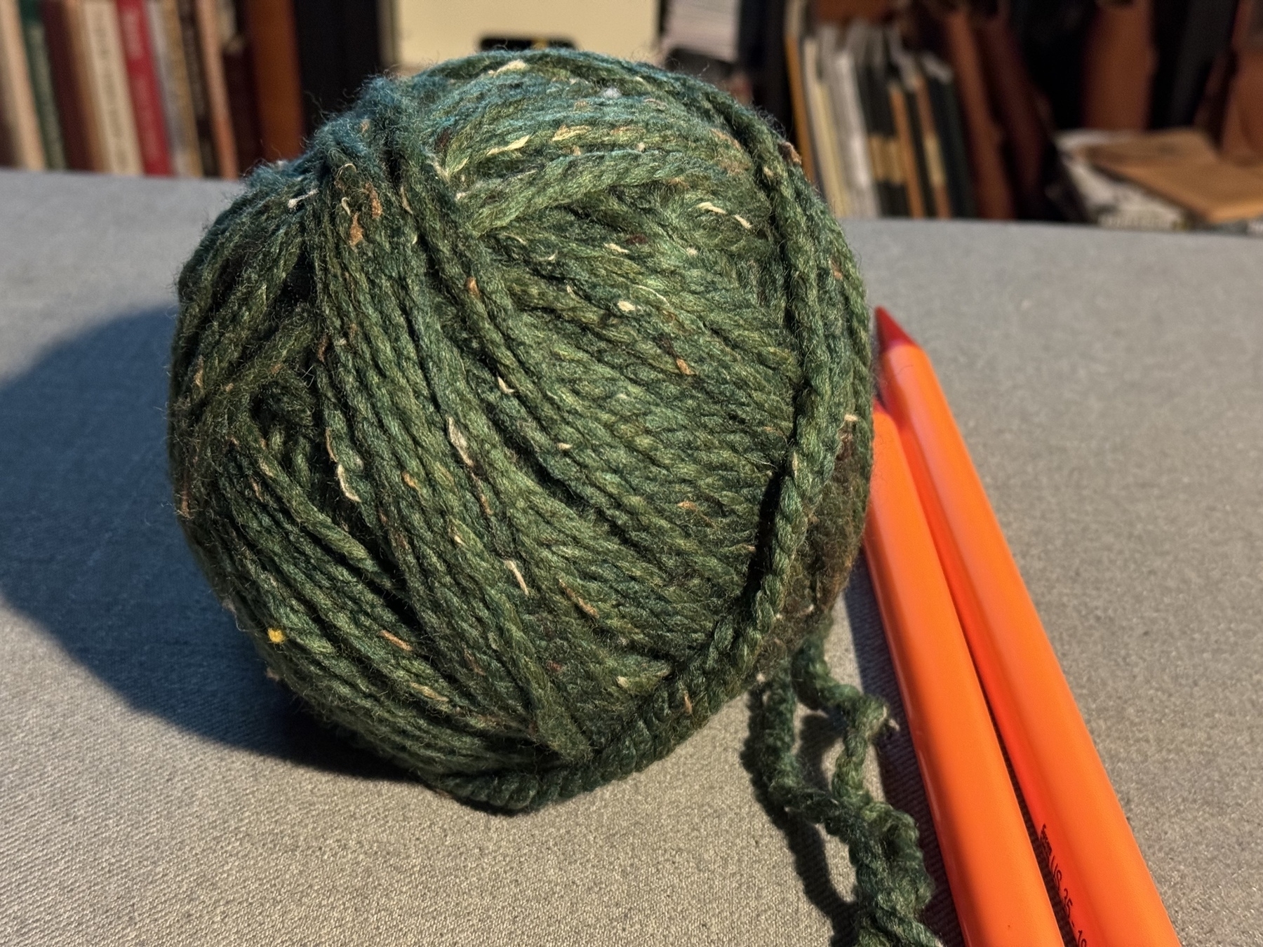 “Kale” colored yarn next to orange knitting needles