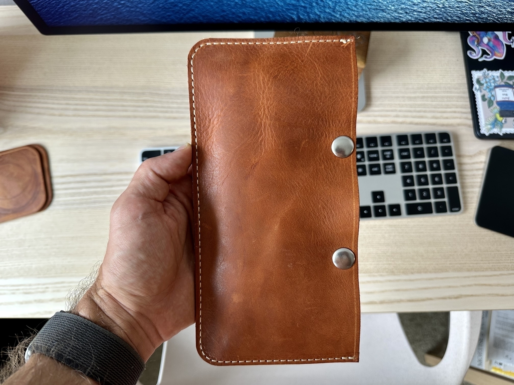 Leather pouch held in one hand showing the clean stitch around the sides and bottom and the two nickel snaps secured on the main top edge. 