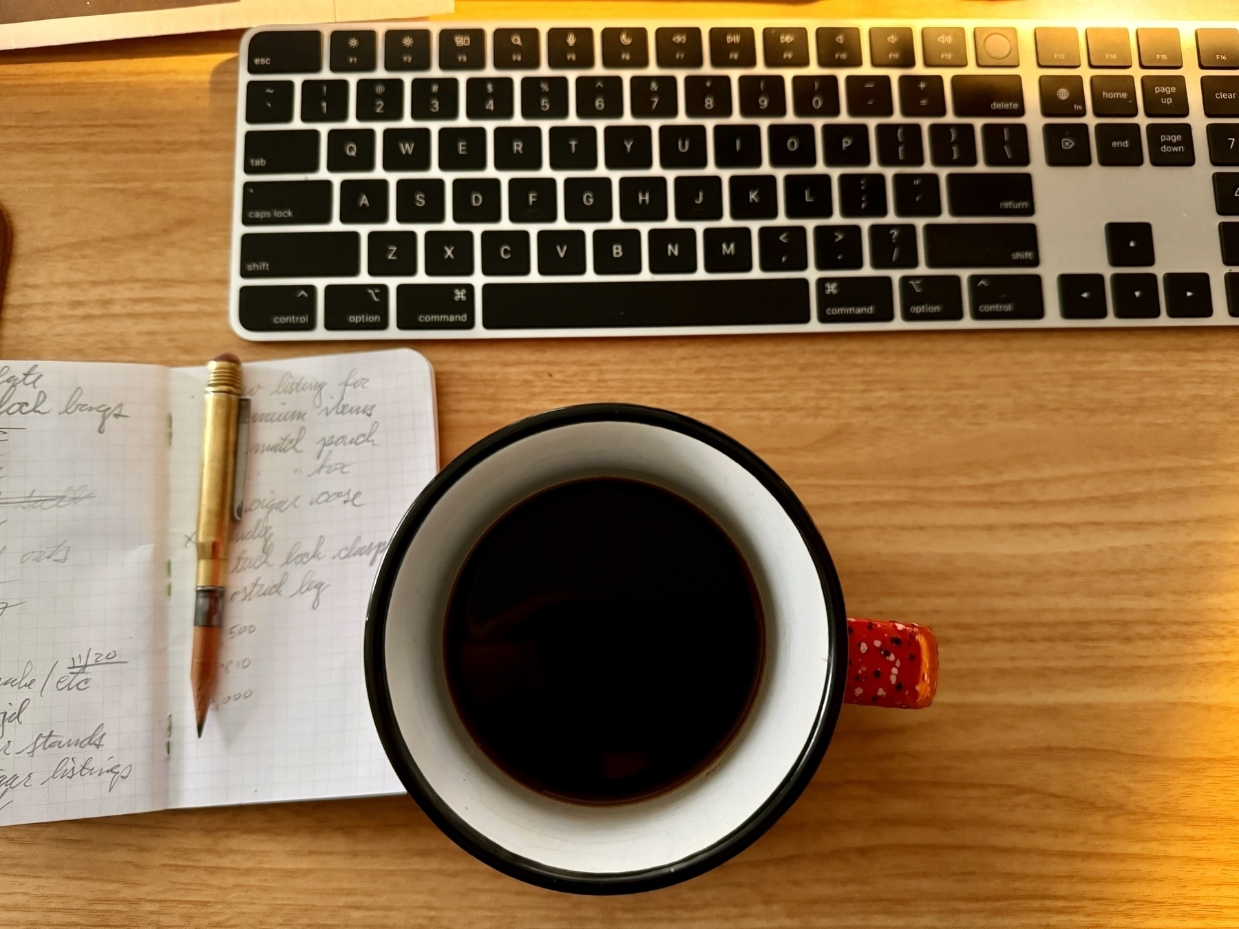 Mug of coffee in front of a computer keyboard with a field notes notebook and pencil on the left. 
