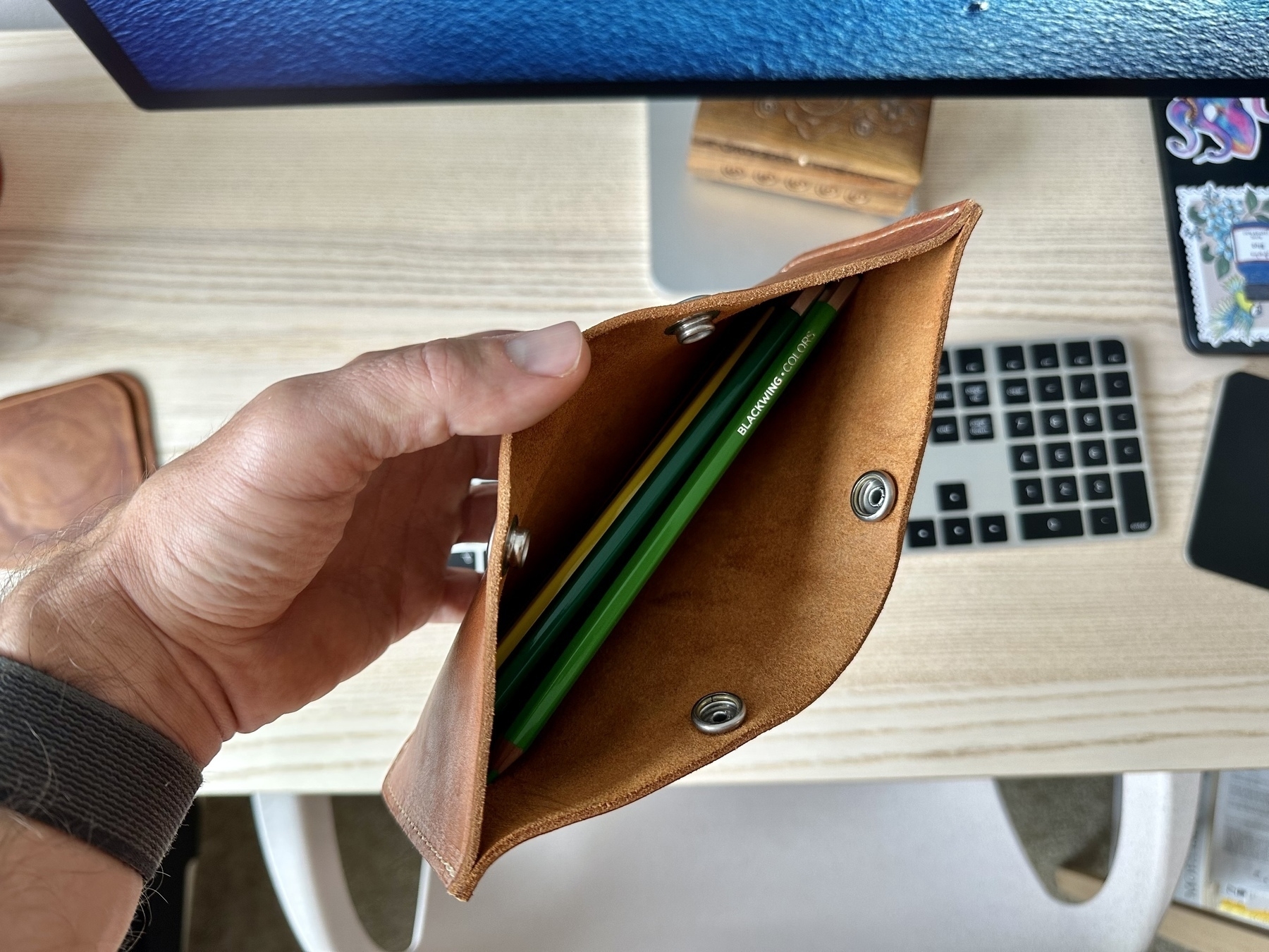 Leather pencil/pen pouch held in hand, the top open so that pencils are seen on the inside of the pouch. 