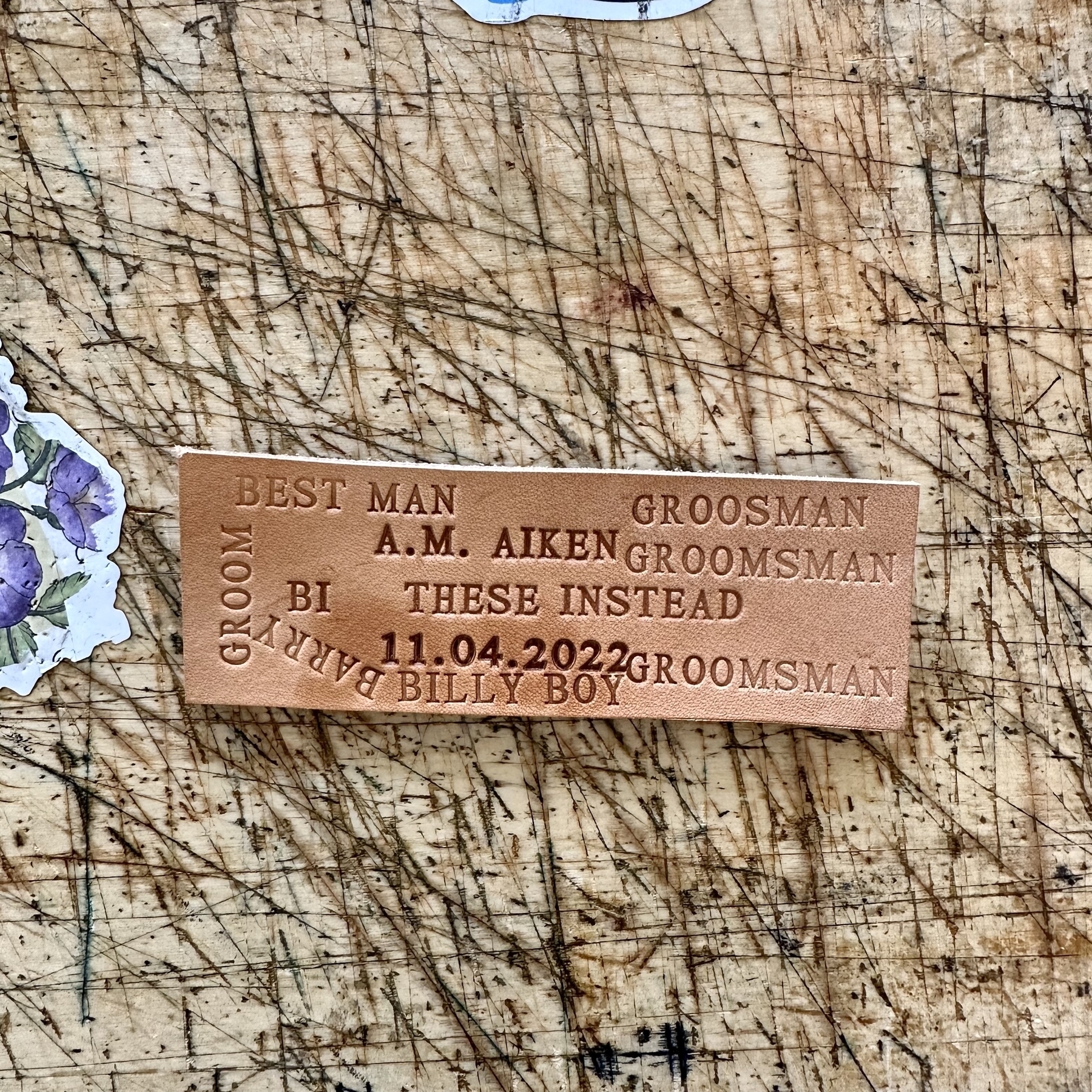 Scrap piece of leather with various stamped words and dates on it, all acting as a test to make sure the stamp is set correctly before placing it permenantly onto a customer's order.