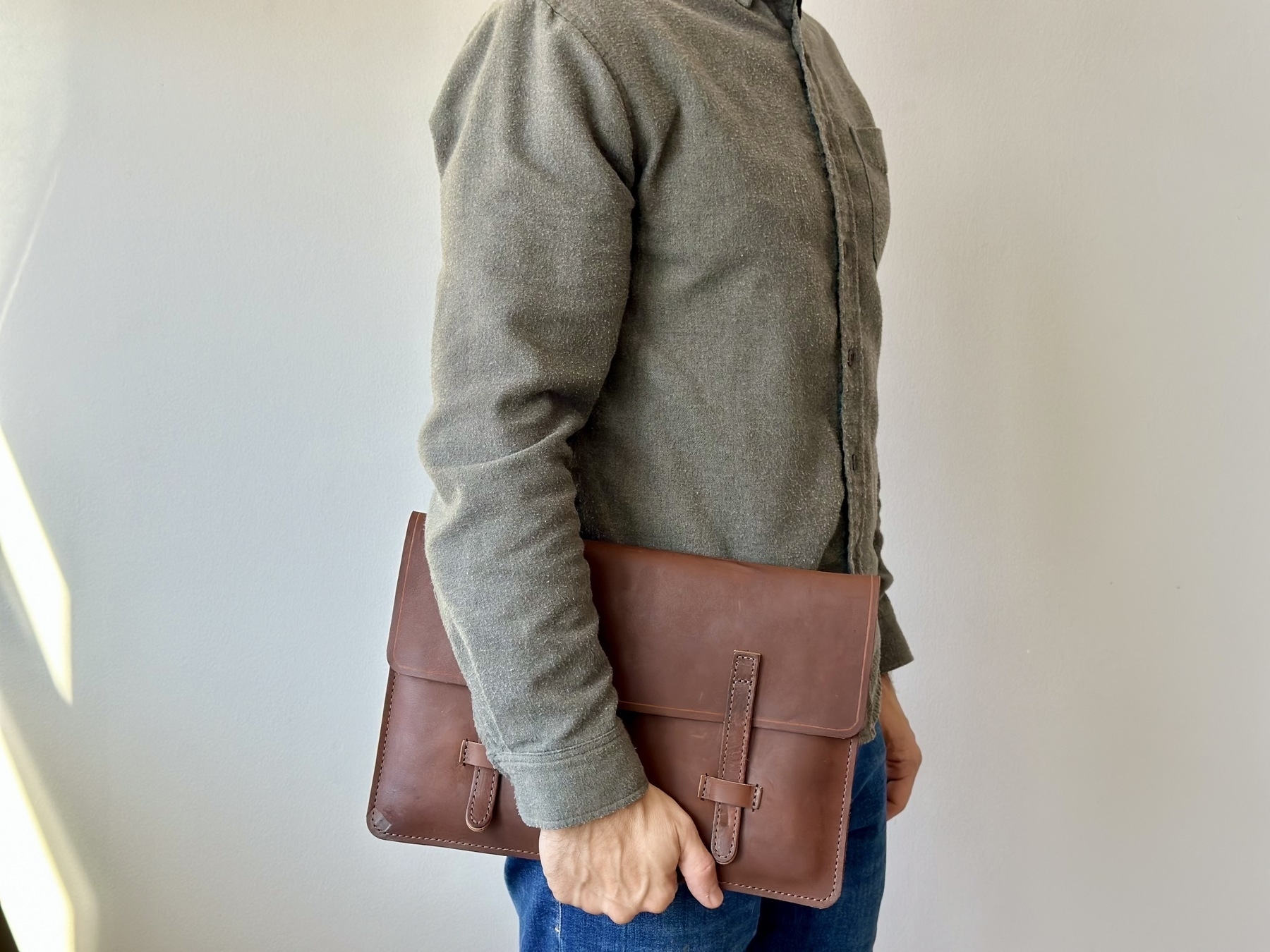 Brown leather laptop sleeve being held in one hand by the waist