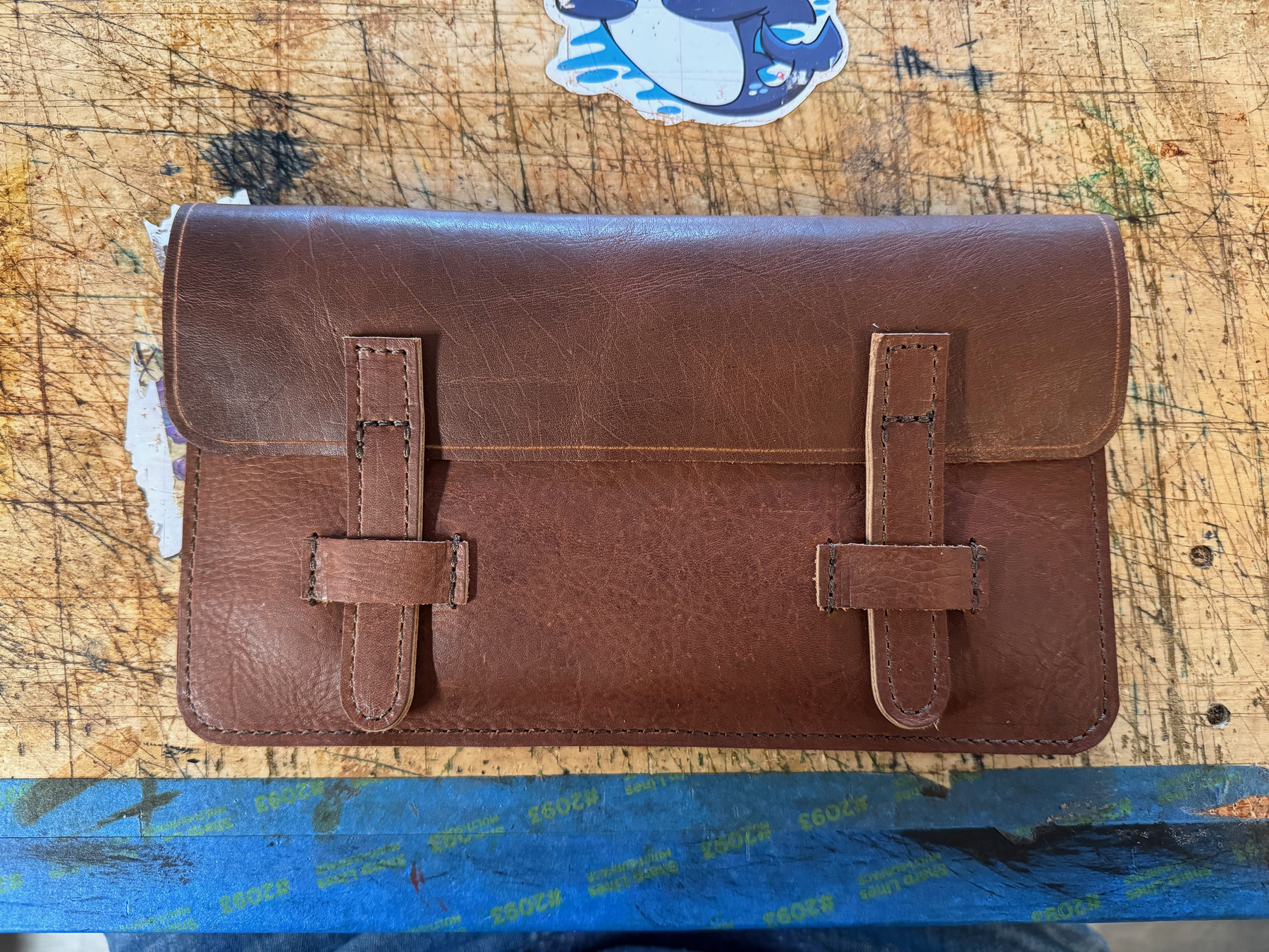 Dark brown Leather pouch shown closed with a flap and two straps
